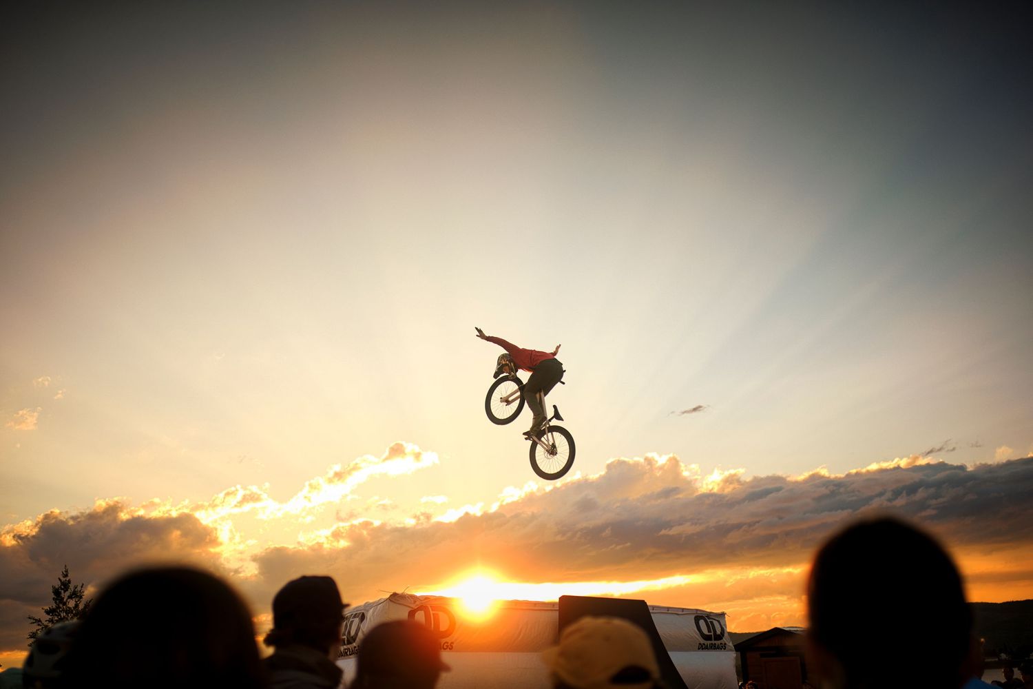 Silhouette of a slopestyle rider performing a no-handed jump trick against a stunning golden sunset by Dave Clément at Sugarloaf bike park.