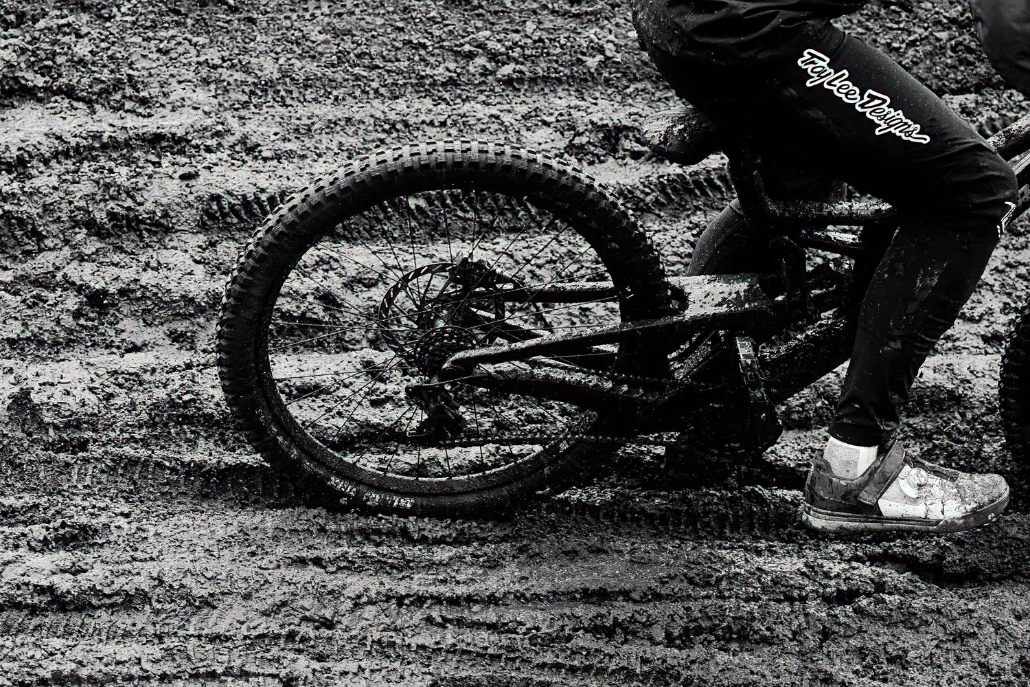 Black and white close-up of mountain bike wheel spinning through thick mud during downhill at Crankworx by Dave Clément, Québec.