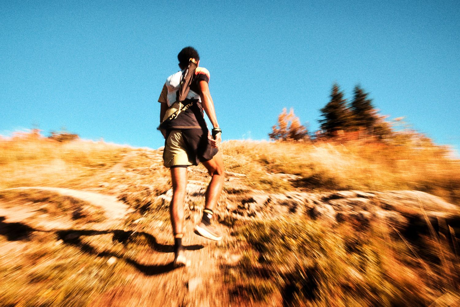A hiker with a backpack climbs a rocky trail under a clear blue sky on a sunny day.