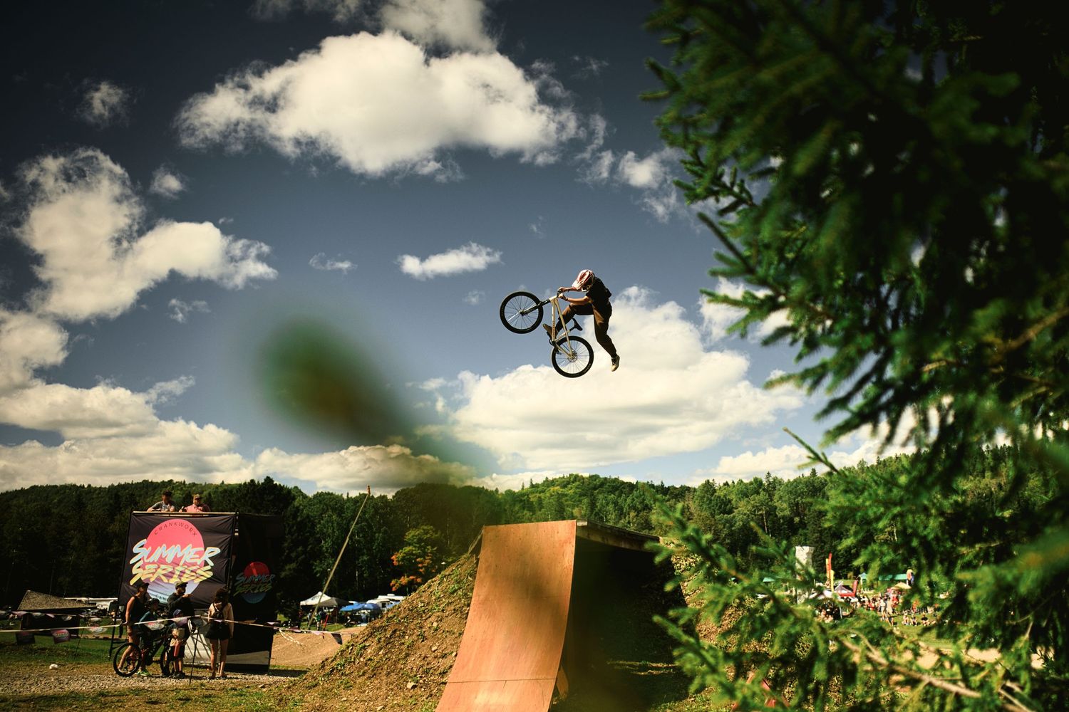 Mountain bike rider performing a massive jump trick over a wooden ramp at Crankworx Summer Series at Sugarloaf by Dave Clément, Québec.