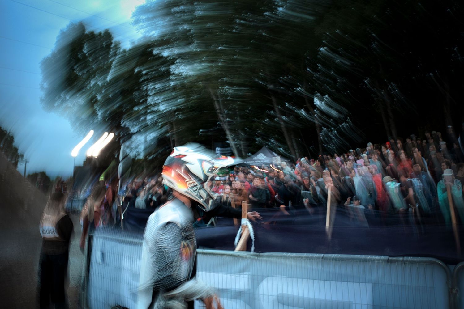 Helmeted cyclist celebrated by cheering crowd at dusk during mountain bike competition event by Dave Clément, Québec.