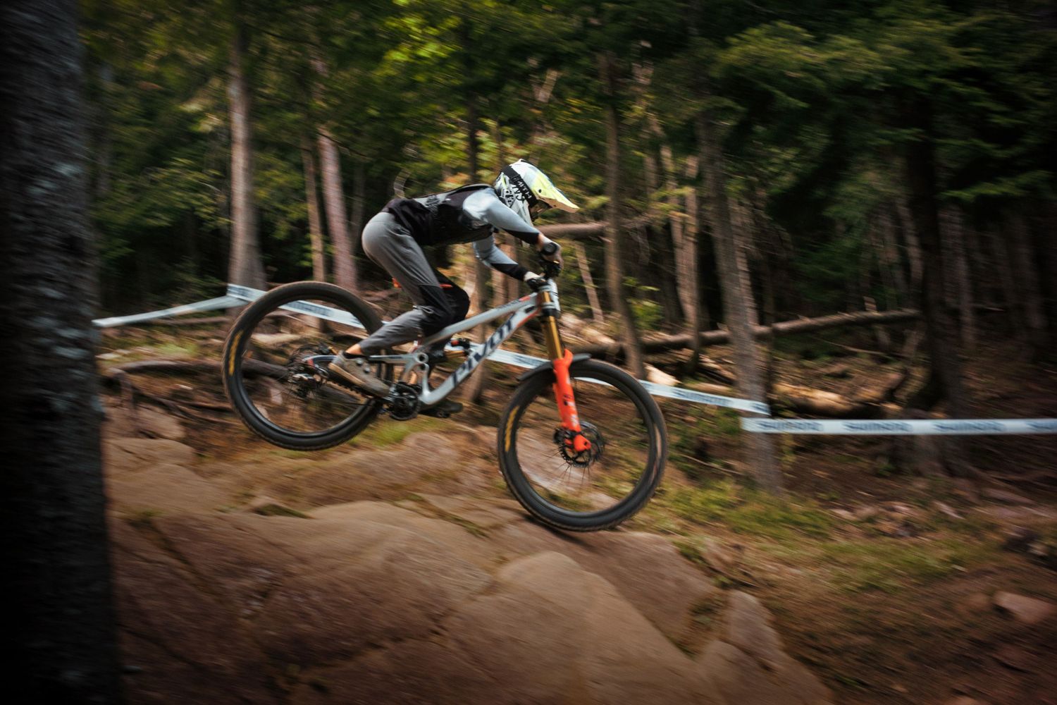 A mountain biker on an Pivot bike flies through a forested trail with motion blur capturing high speed by Dave Clément, Québec.
