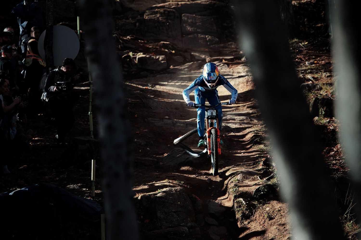 Ronan Dunne in blue gear descends a rocky forest trail during a downhill race with his rear tire out of the rim by Dave Clément, Québec.