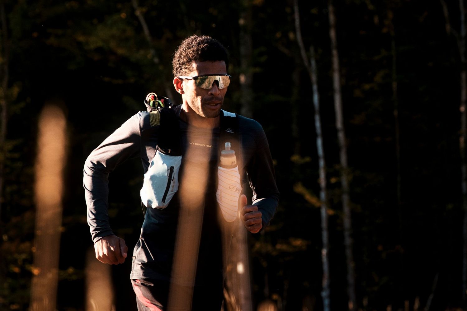 A hiker with sunglasses and backpack runs through a dark forest trail in autumn.