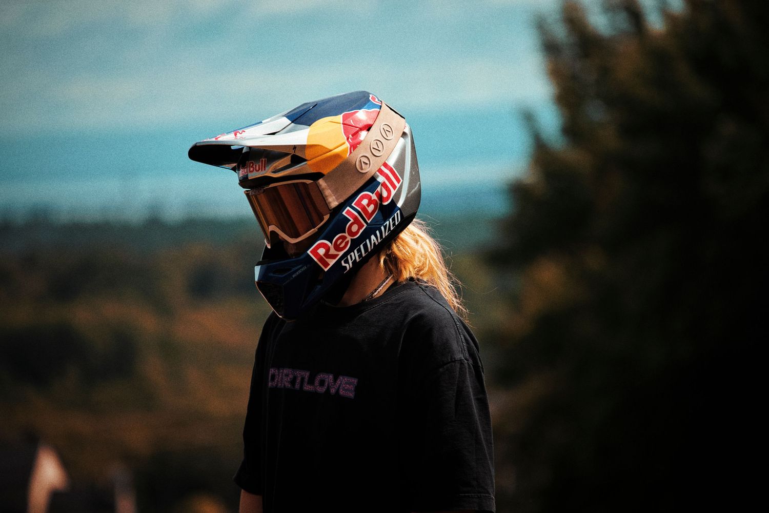 Female rider wearing a Red Bull sponsored helmet with long blonde hair outdoors by Dave Clément, Québec.