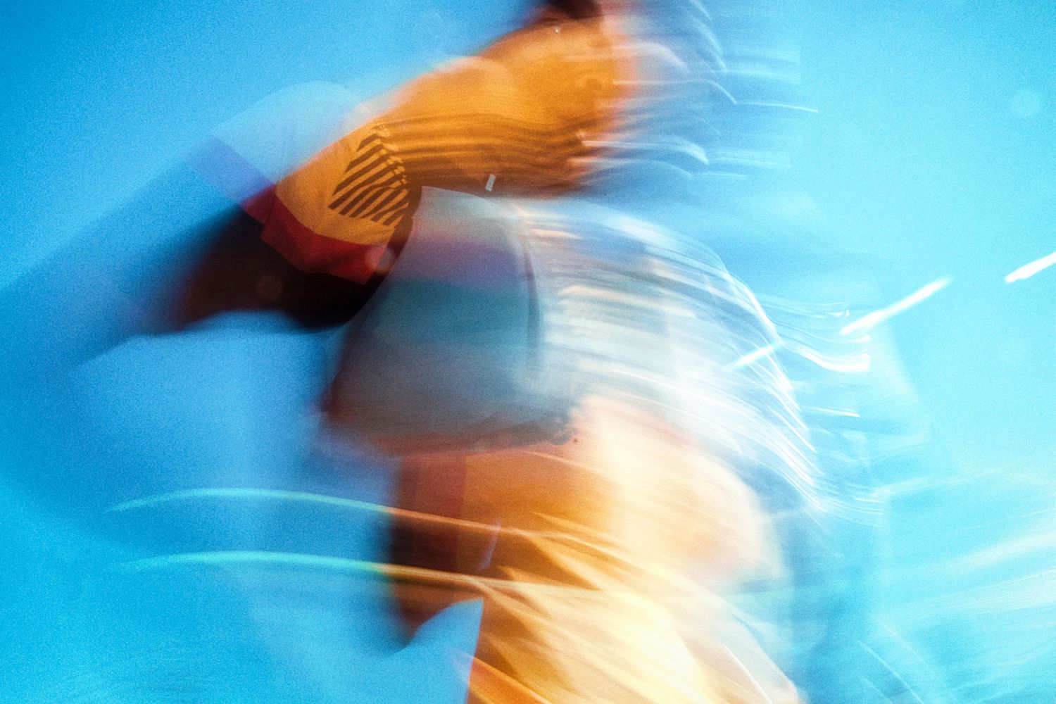 Blurred motion photograph of an athlete in orange and black sportswear against a vivid blue background.