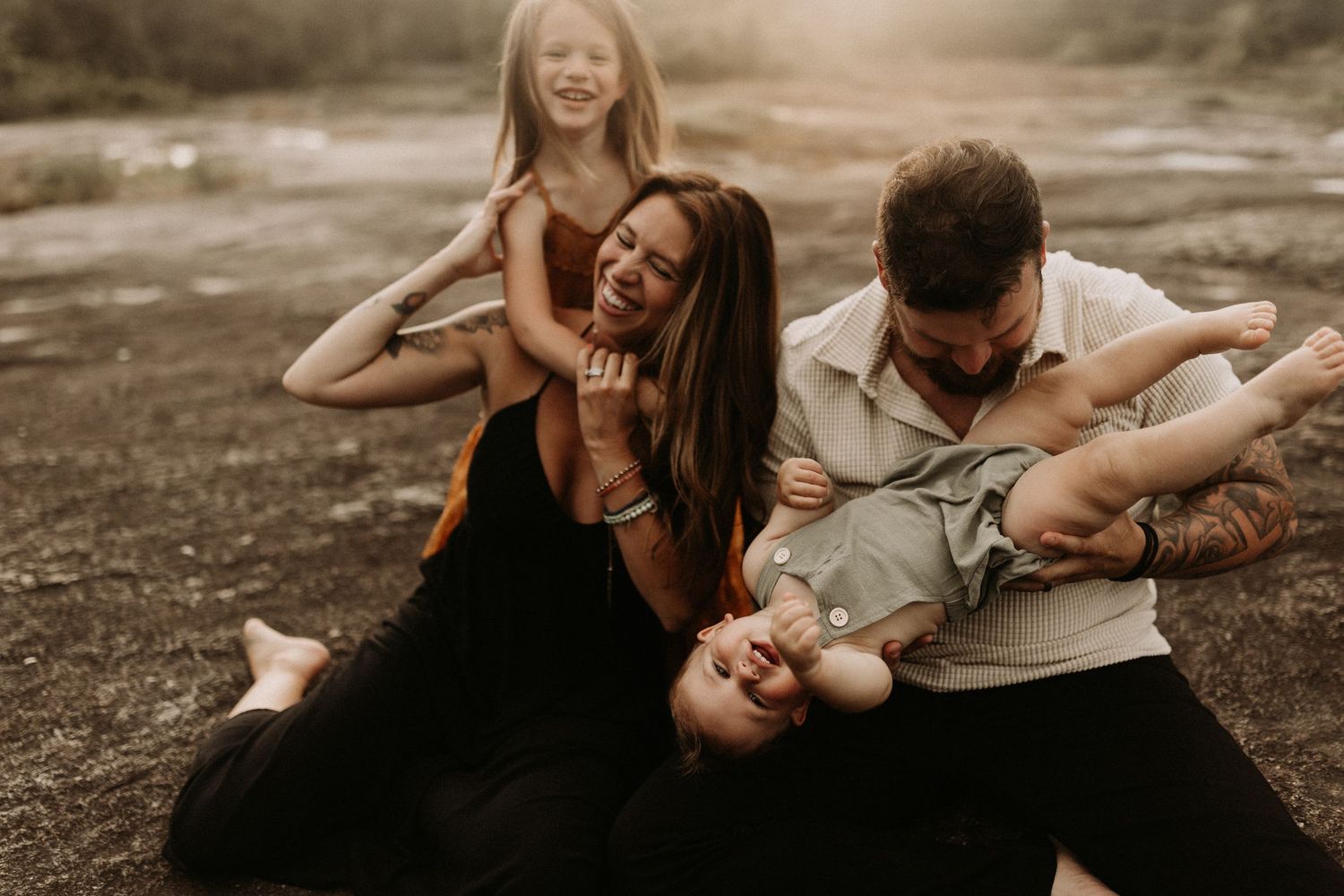 Joyful family of four laughing and playing together outdoors in warm sunset light.