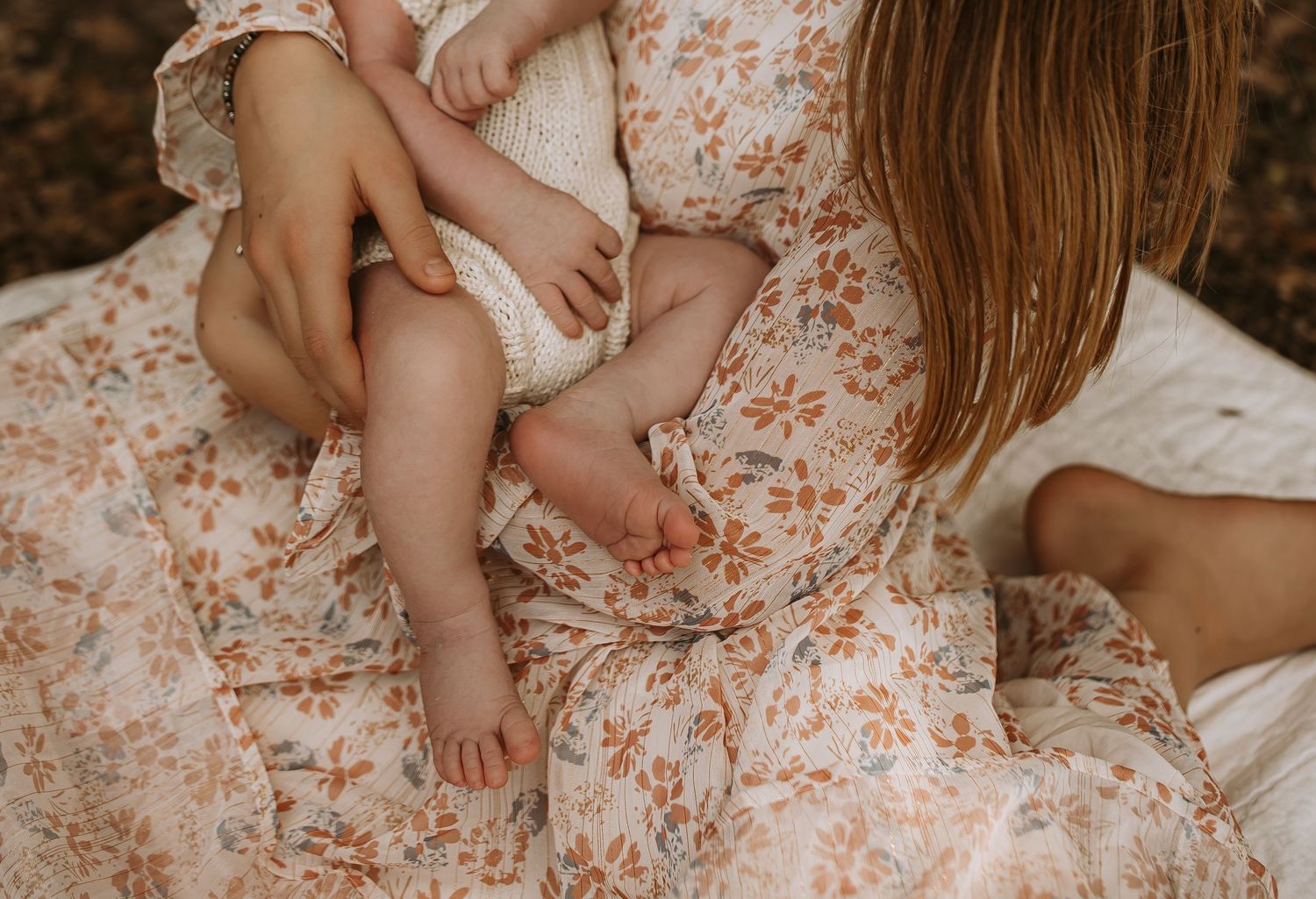 Close-up of mother in floral dress cradling newborn baby on her lap outdoors.