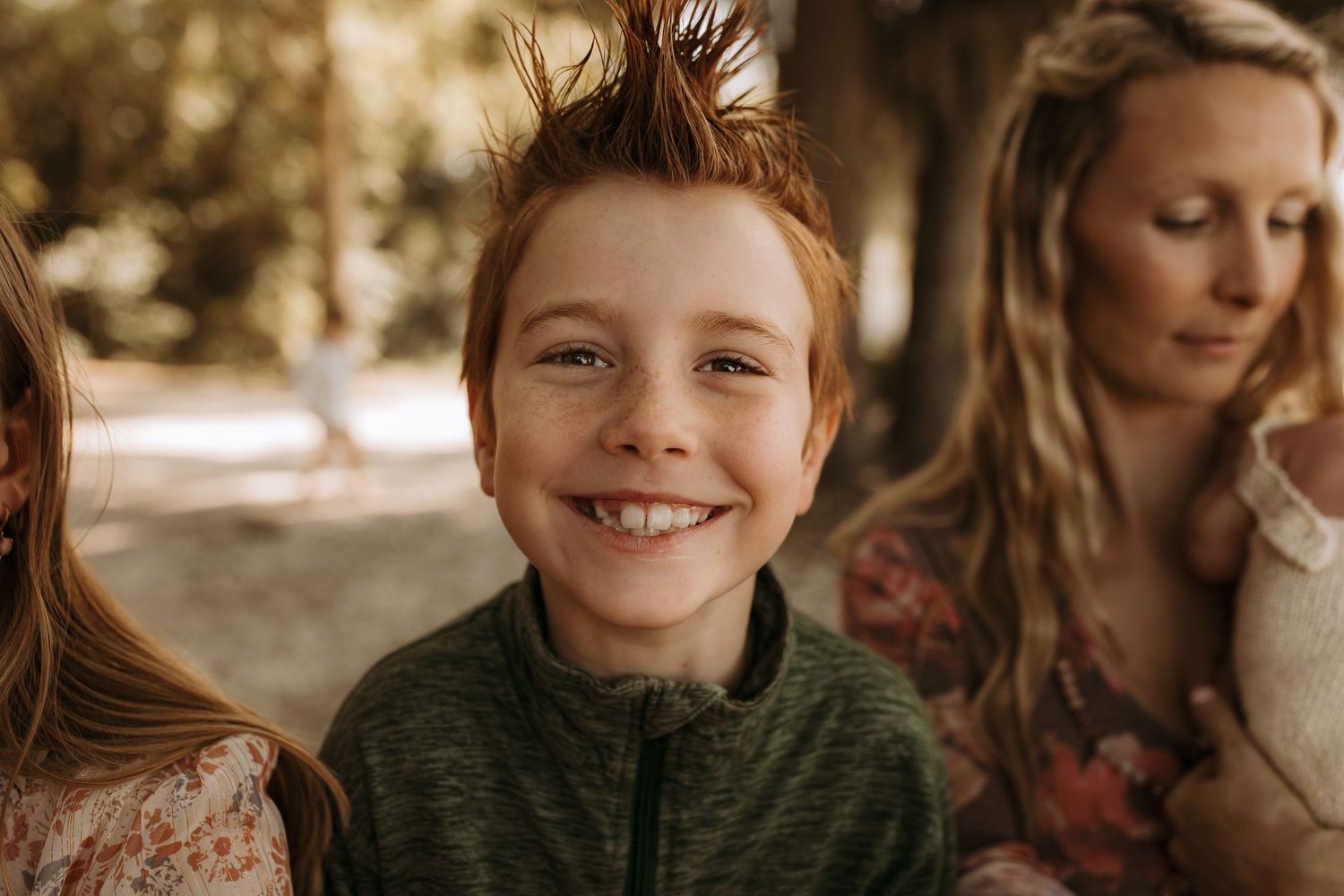Smiling red-haired boy with a mohawk hairstyle poses outdoors with family members in a candid photo.