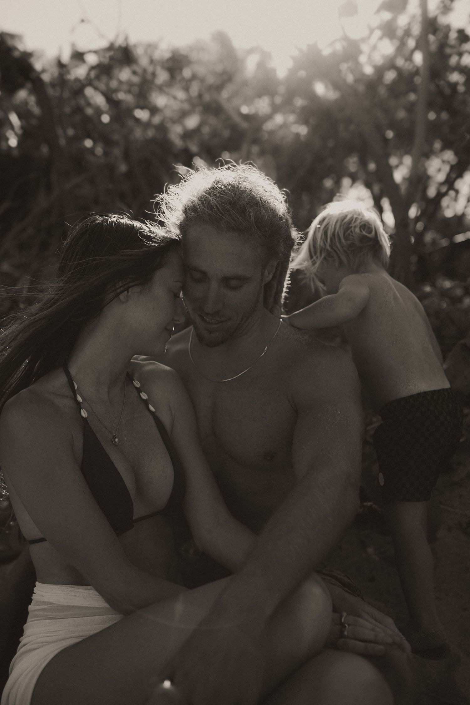 Black and white photo of a couple and child sharing a tender moment outdoors in nature.