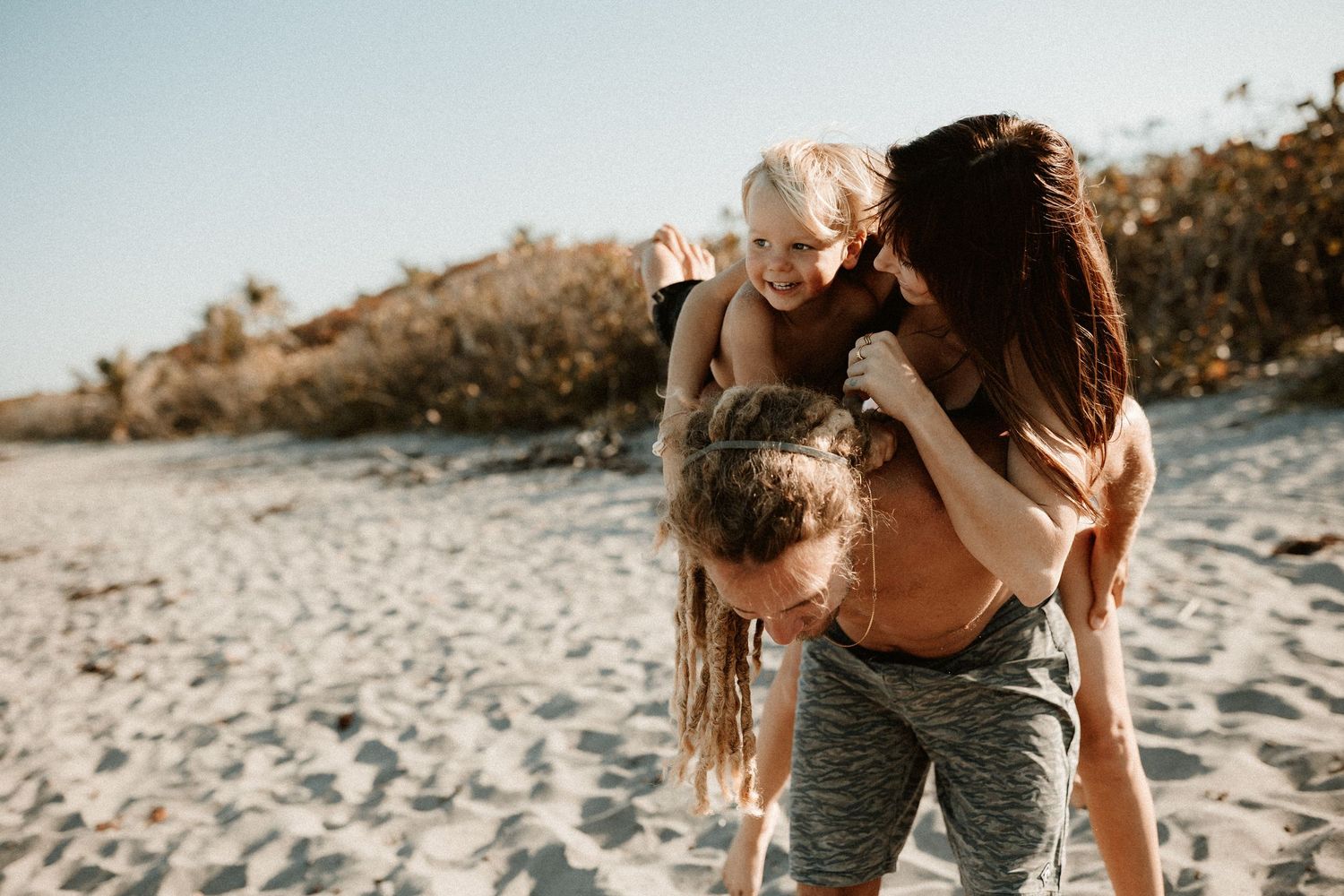 Happy family with young child playing on a sunny sandy beach together.