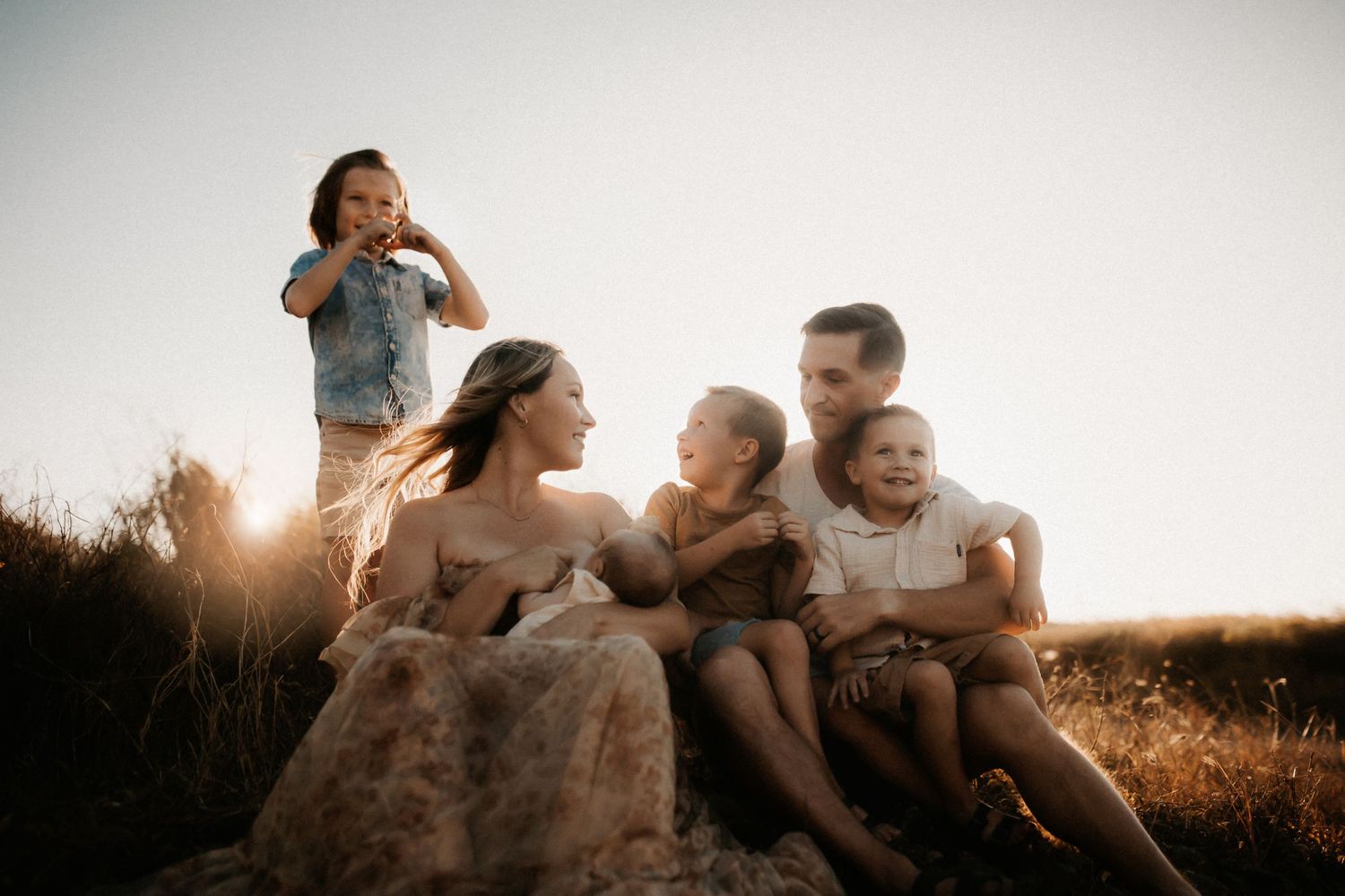 Happy family of five relaxing on rocks in golden sunset light, with children laughing and playing outdoors.