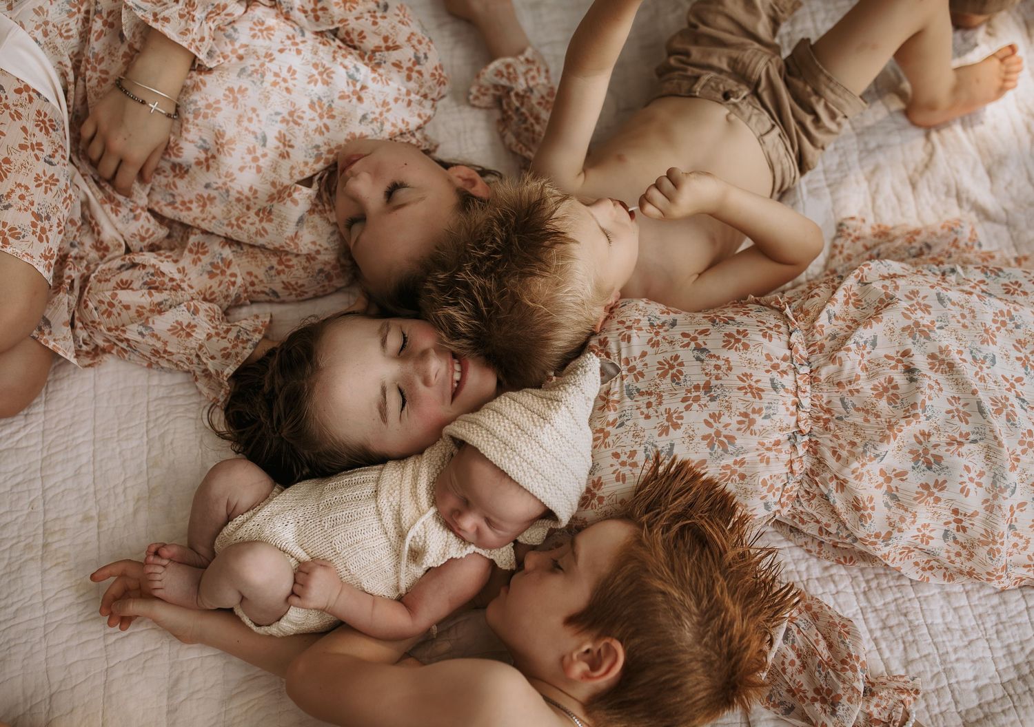 Four young children sleeping peacefully together on a white bed, wearing floral outfits in a cozy family nap scene.