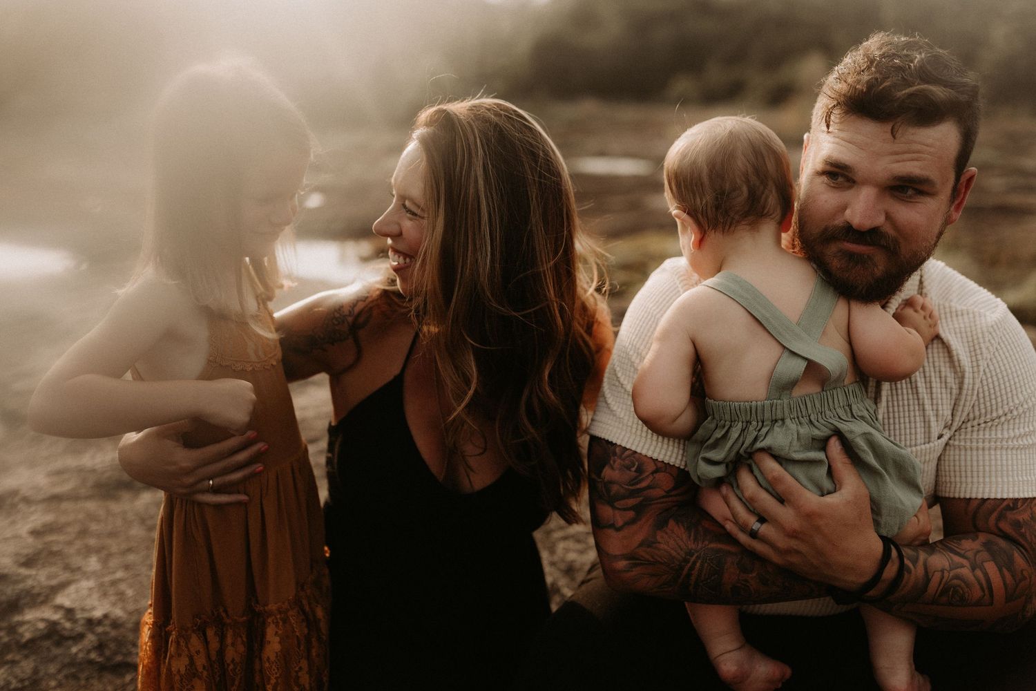 Tattooed couple with two young children enjoying a warm golden hour outdoor family photo session.
