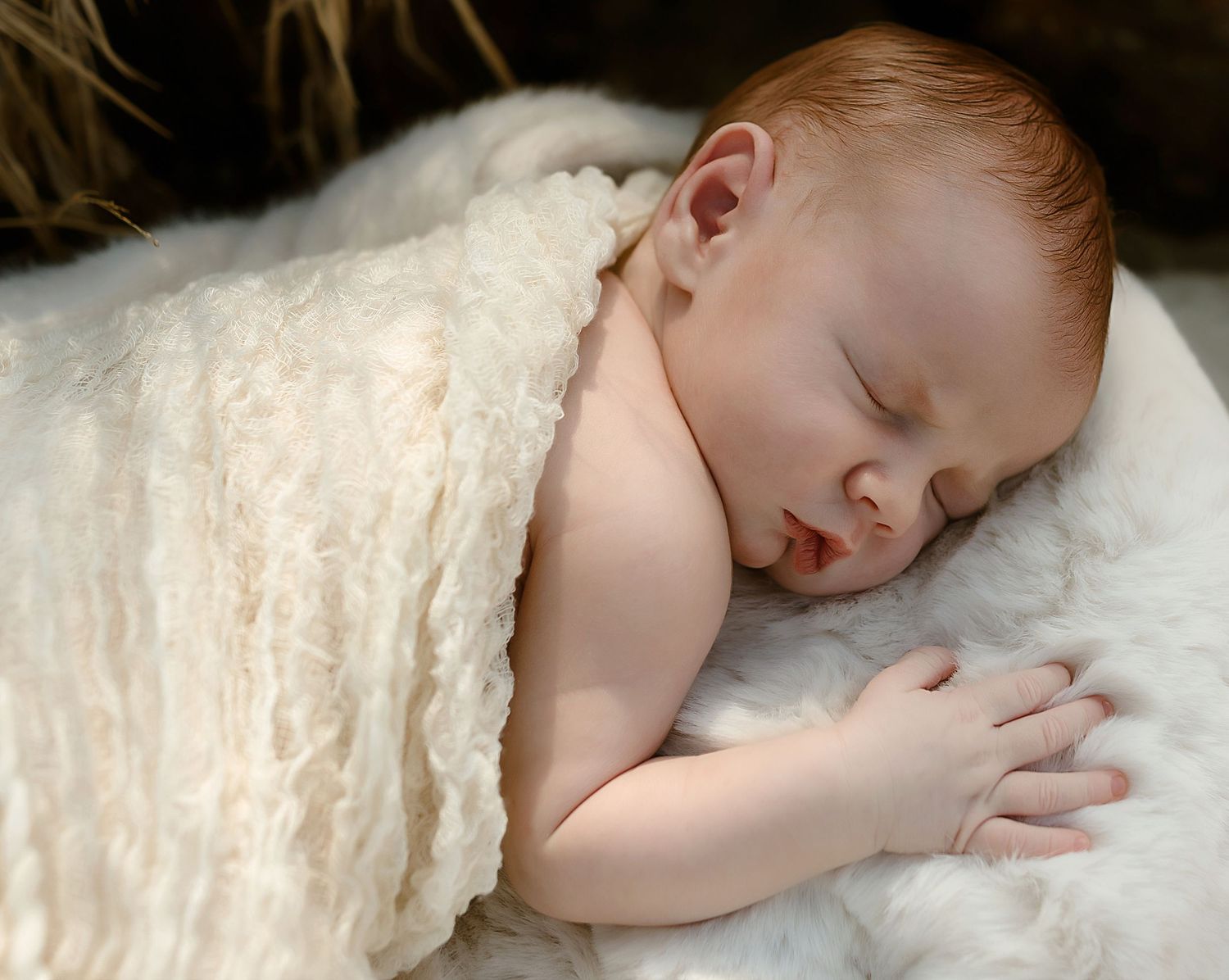 A peaceful newborn baby sleeps wrapped in a soft cream blanket on a fluffy white surface.