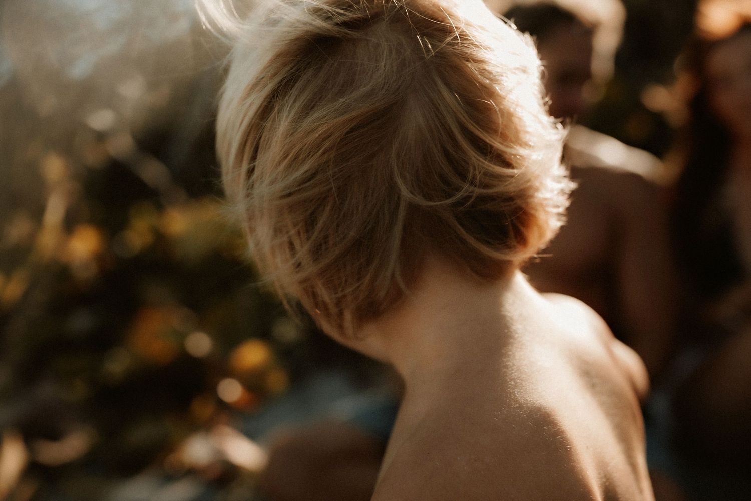 Close-up back view of a young blonde child with short hair in warm golden sunlight outdoors.