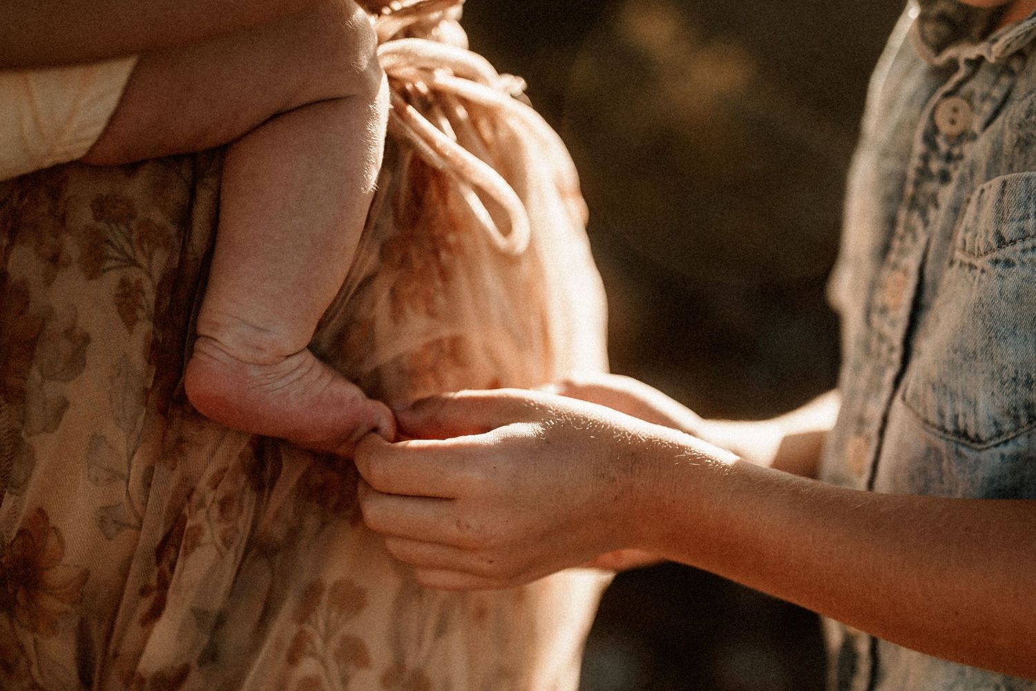 Close-up of two adults gently holding a baby's tiny feet in warm golden outdoor light.