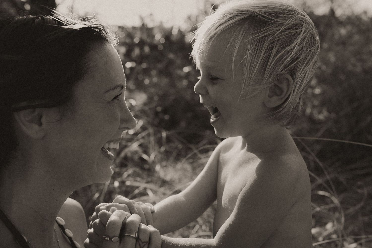 Black and white photo of a mother and happy toddler sharing a joyful moment face to face outdoors.