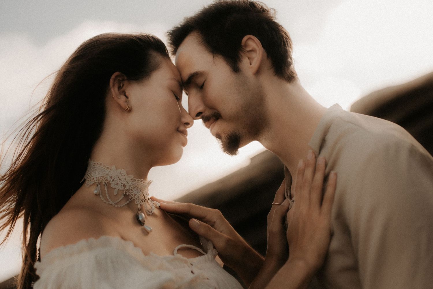 Romantic couple sharing an intimate moment, foreheads touching, soft natural light, wedding attire, tender embrace outdoors.