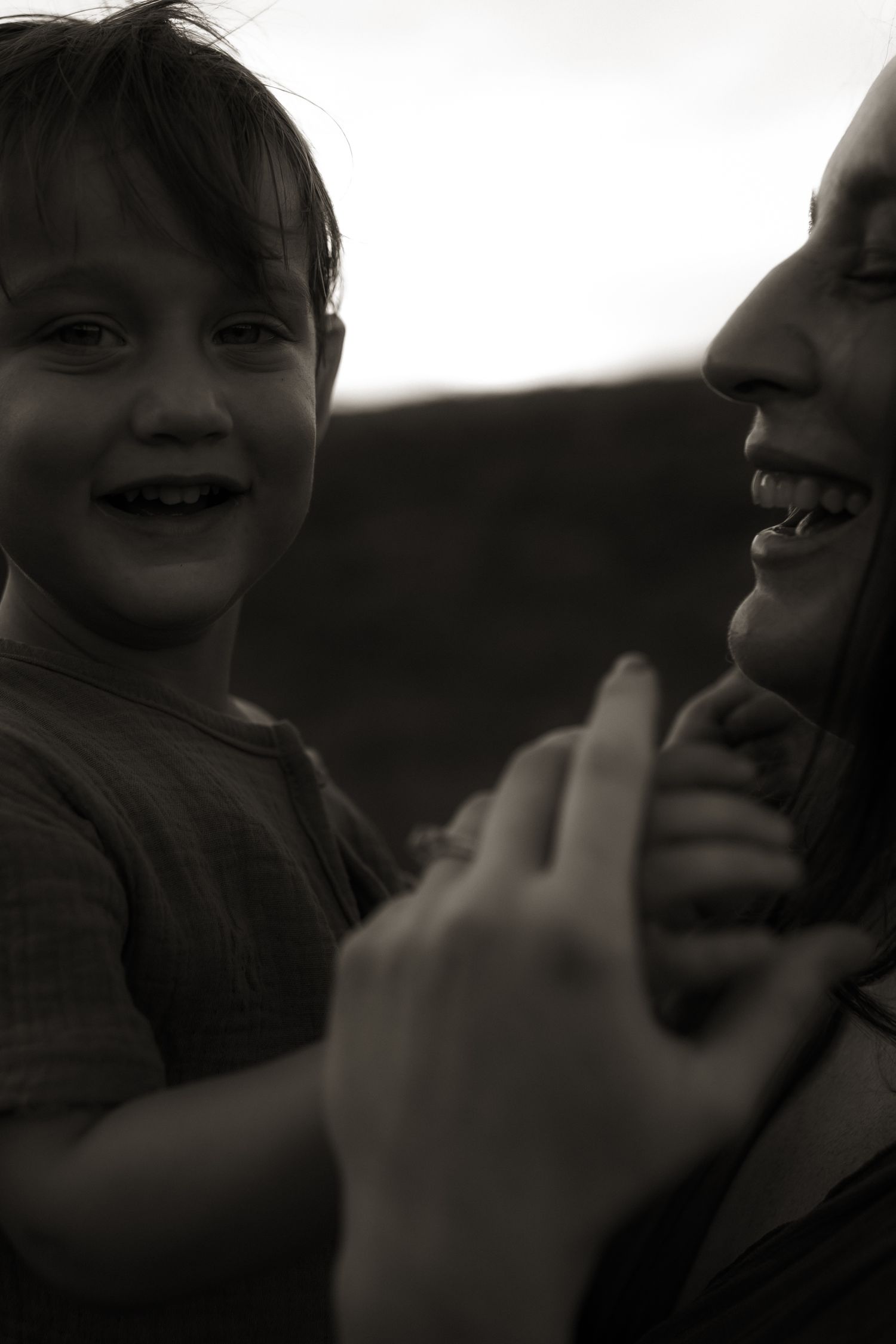 A black and white photo of a laughing child and woman holding hands together.