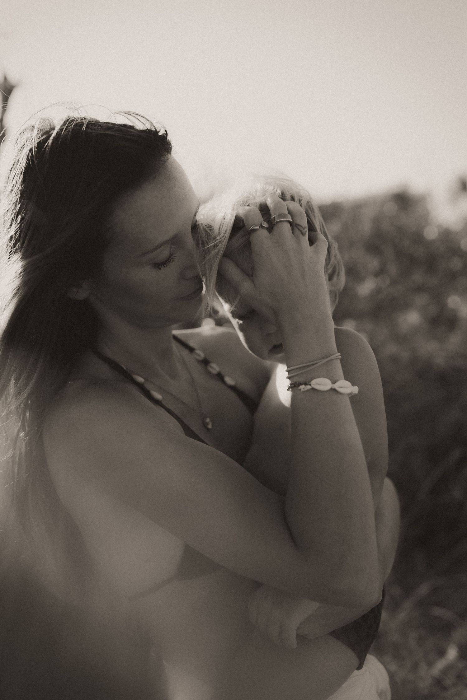 Black and white photo of a woman holding a seashell to her face outdoors, wearing jewelry and a necklace.