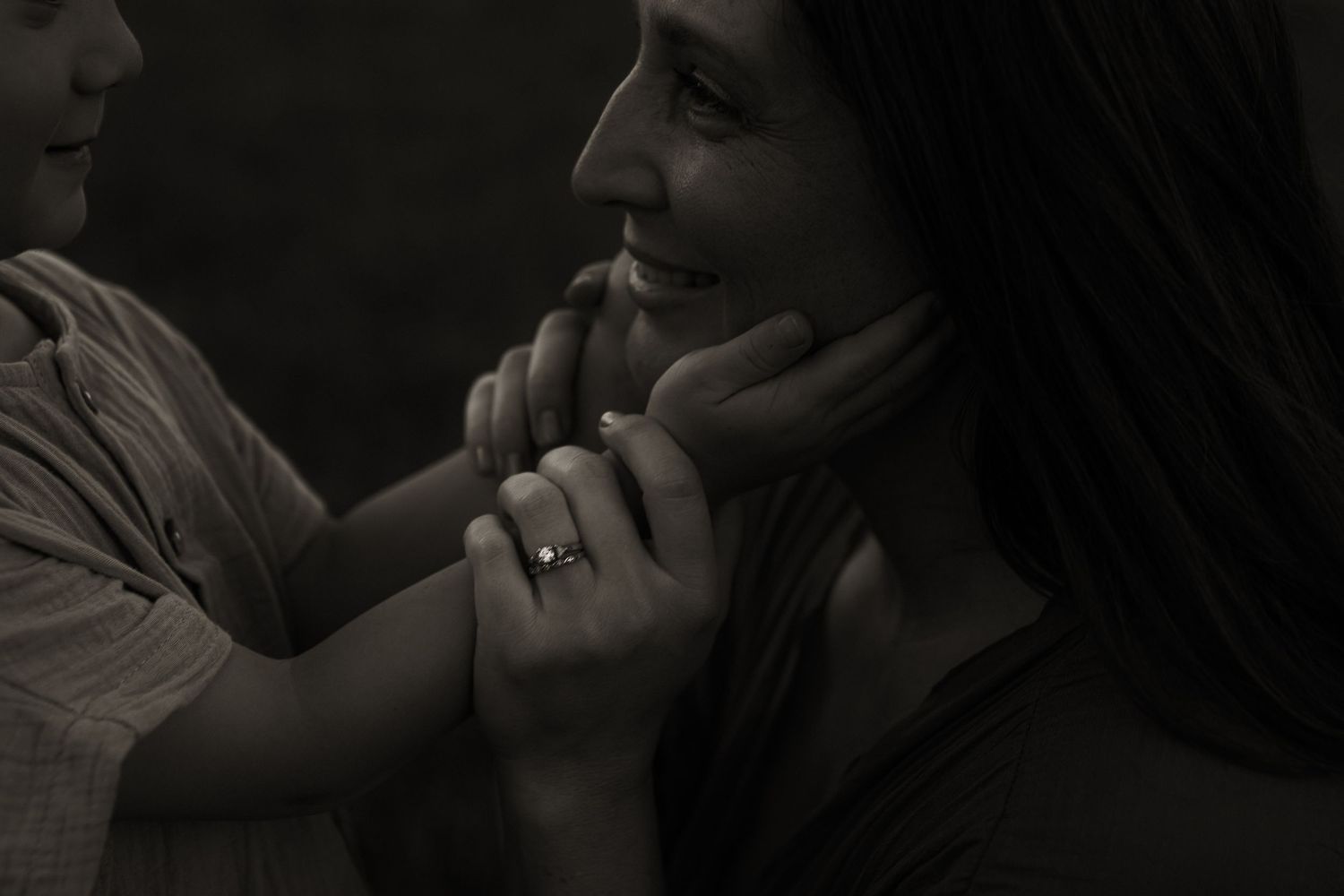 Black and white photo of a smiling woman and child holding hands tenderly, wearing a diamond ring.