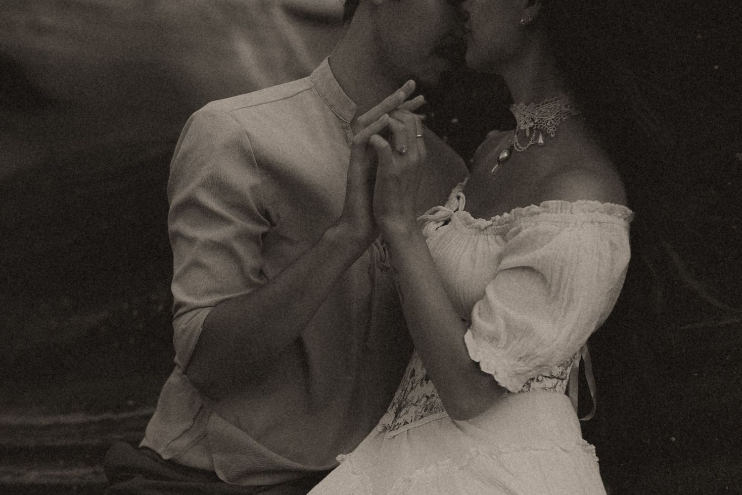 Vintage black and white photo of a couple sharing a romantic kiss while holding hands in wedding attire.