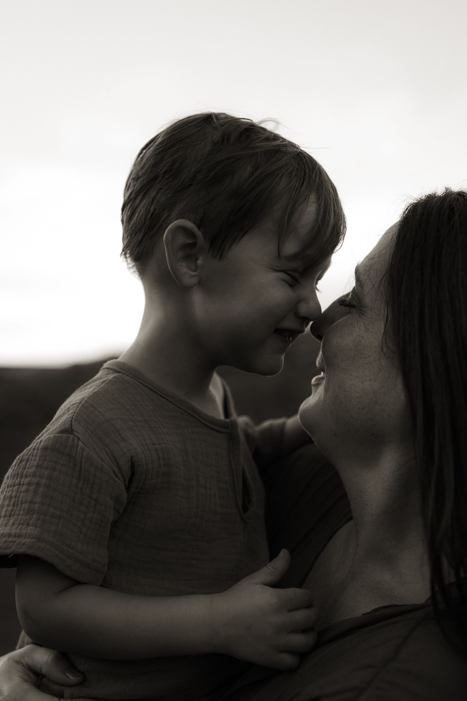 Black and white photo of mother and young son touching noses, smiling tenderly.