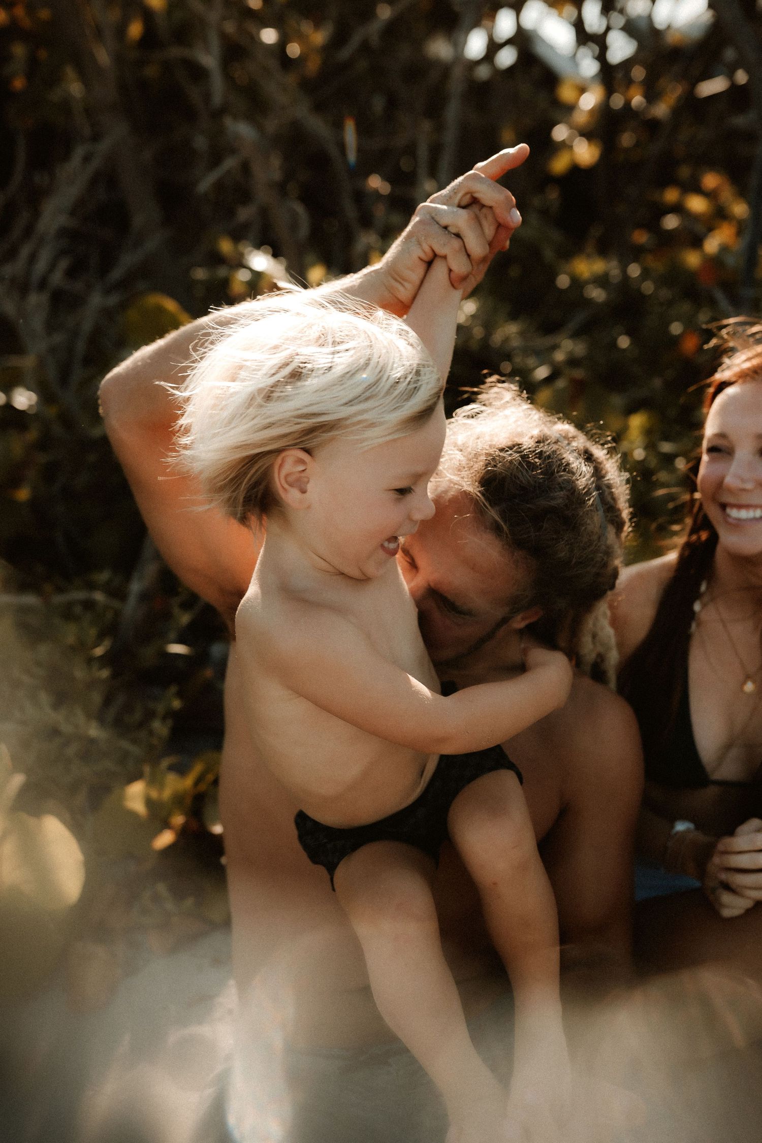 Family enjoying a sunny day outdoors, father kissing toddler while mother smiles nearby.