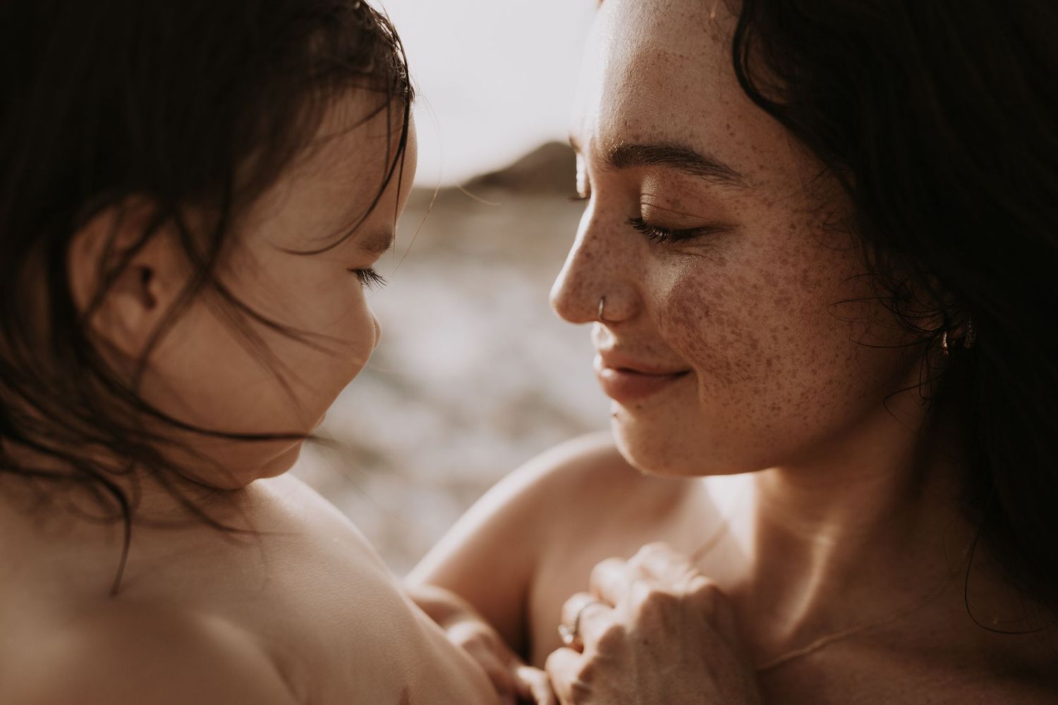 Close-up of freckled mother tenderly holding baby, warm golden light, intimate moment.