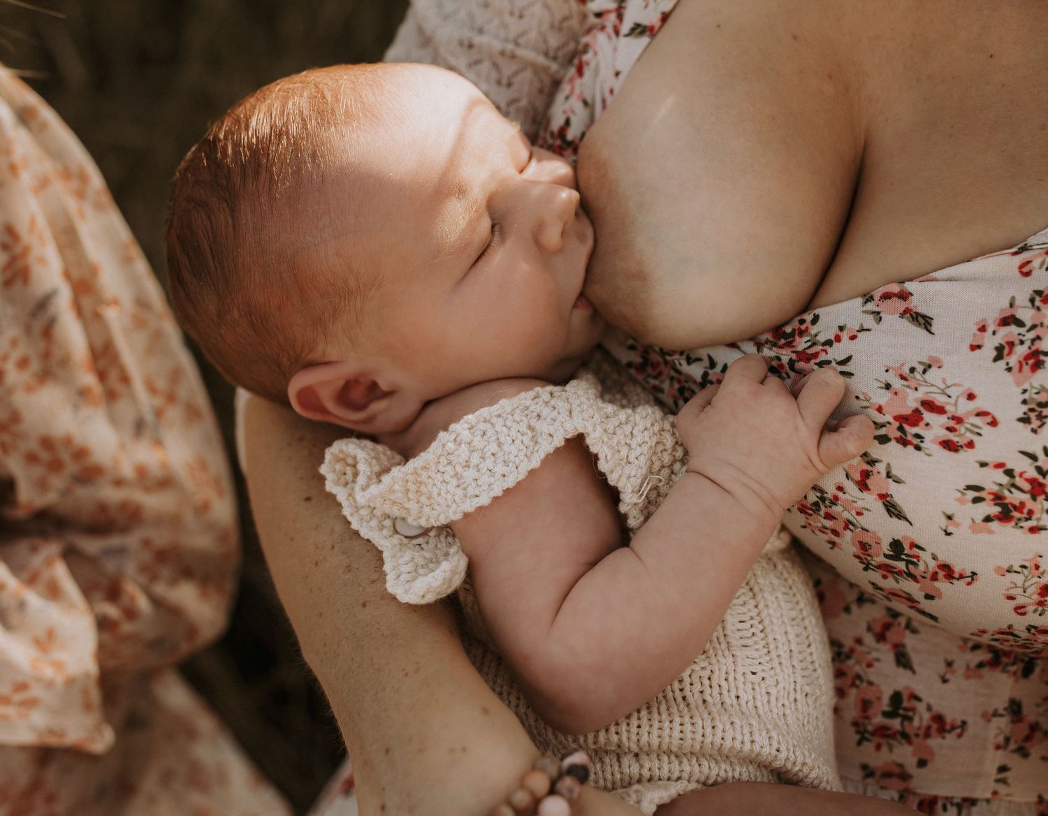 Newborn baby breastfeeding while cradled in mother's arms, wearing a knit outfit.