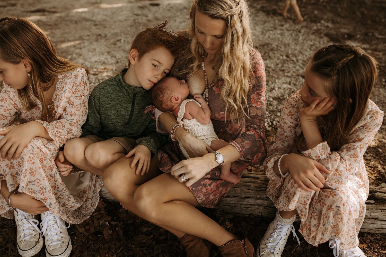 Blonde mother sits with four children admiring newborn baby in a warm outdoor family portrait.
