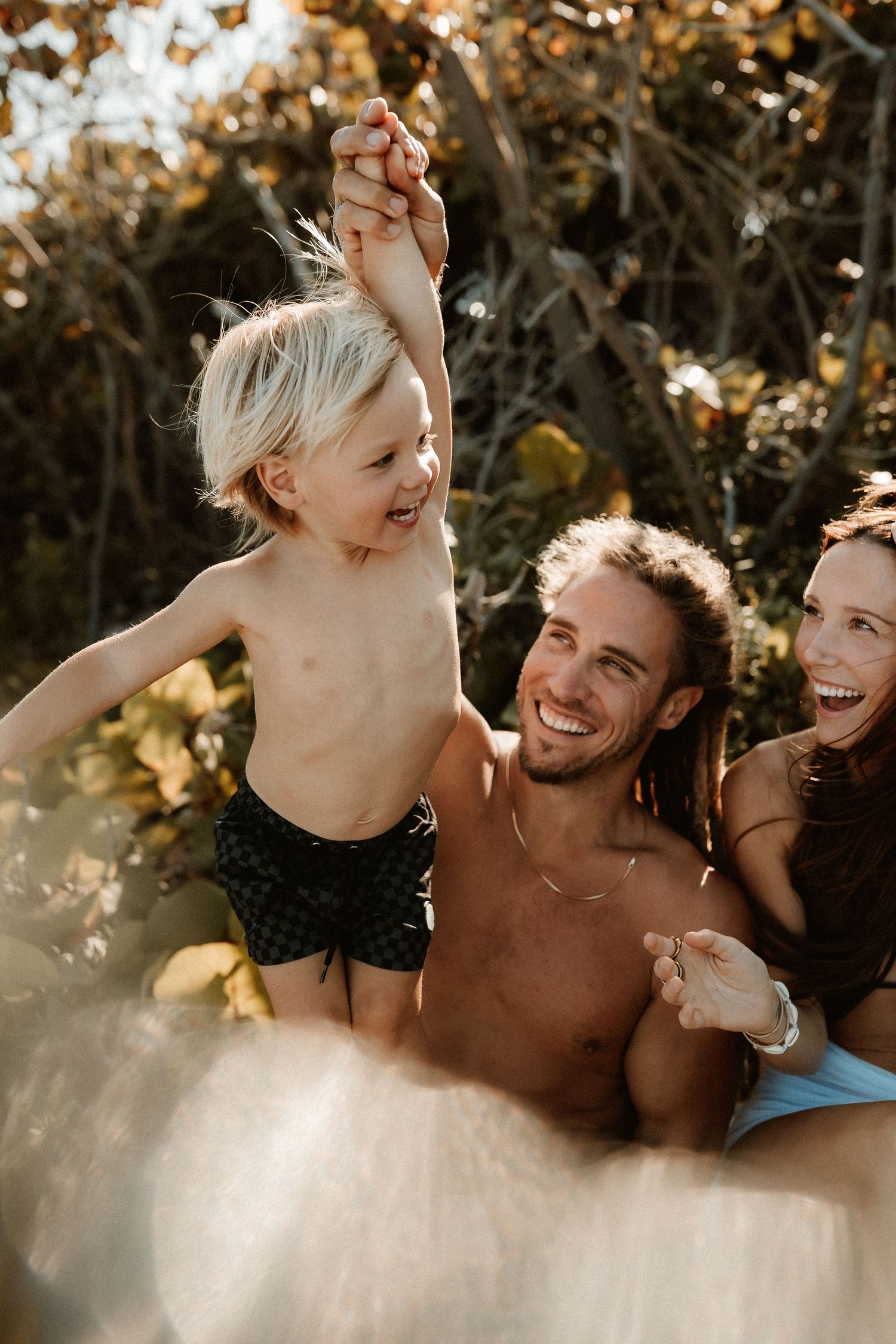 Happy family with young blonde child laughing outdoors in golden sunlight.