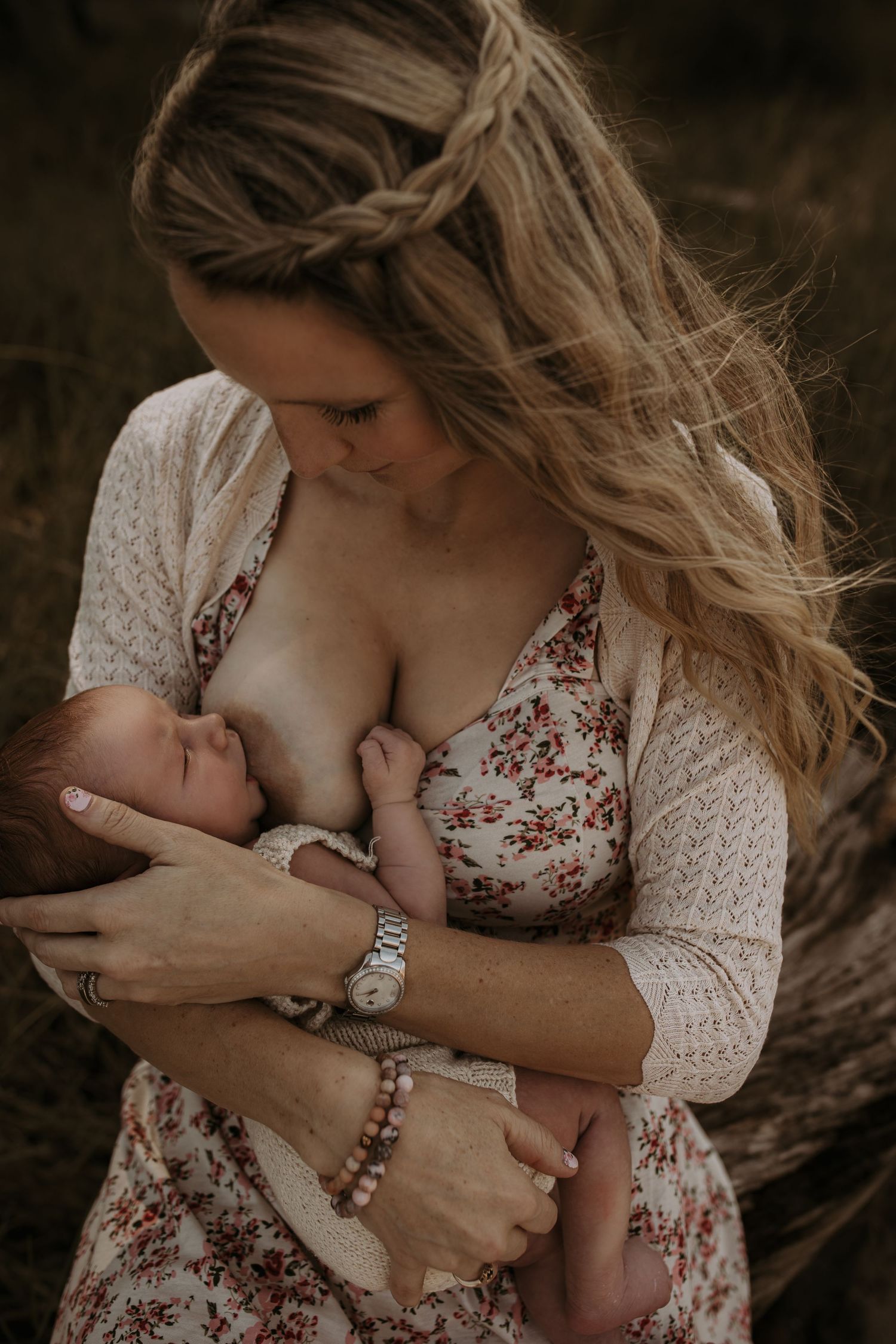 Mother breastfeeding newborn baby outdoors in natural setting wearing floral dress.