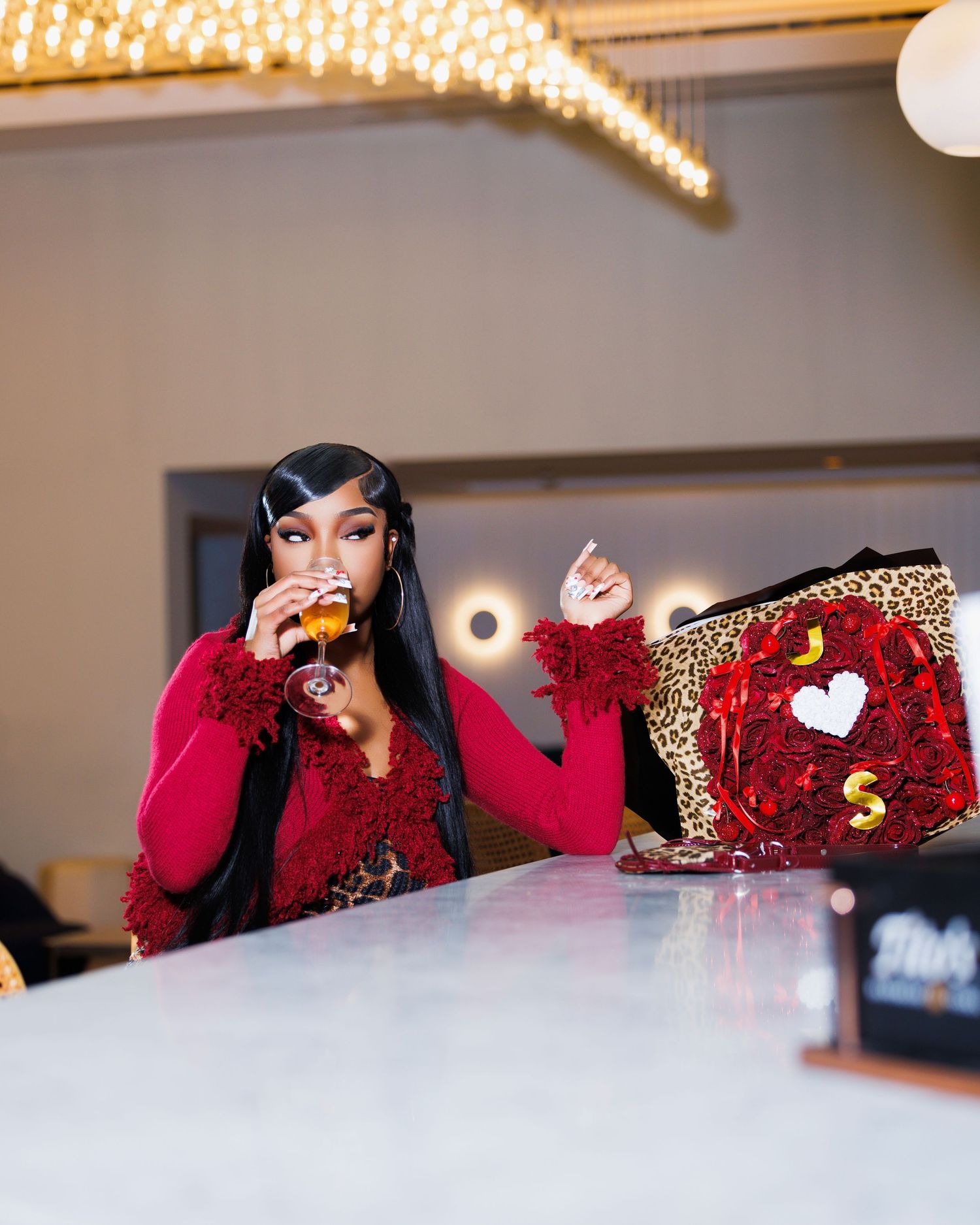 Woman in red fringe top sipping a drink at a bar beside a decorative leopard print bag with red roses.