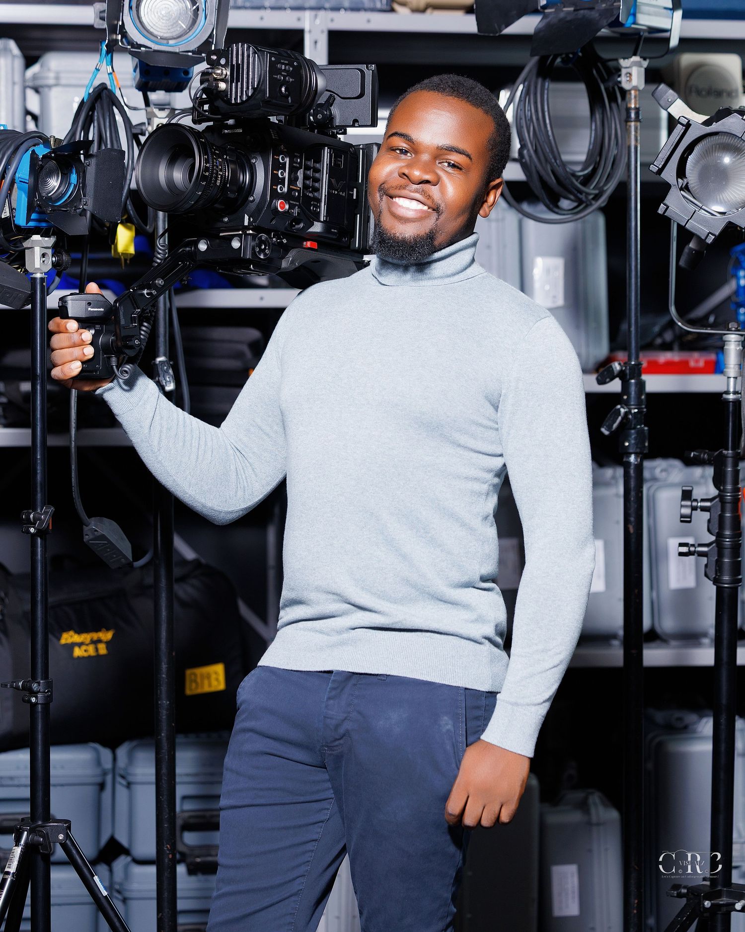 Smiling man in gray turtleneck holding professional film camera in a photography studio with lighting equipment.