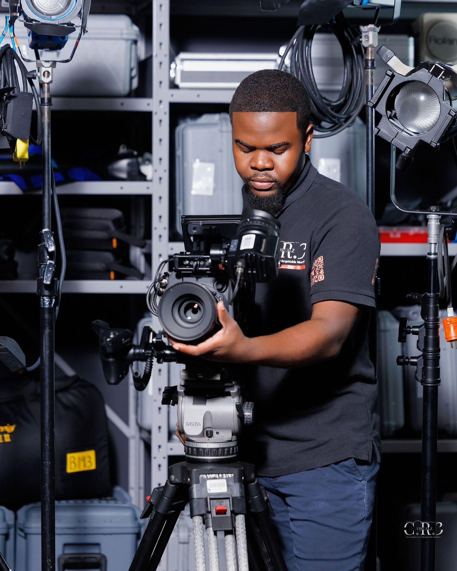 A videographer adjusts a professional camera on a tripod in a well-equipped film studio surrounded by lighting gear. Built for Brands. Miami