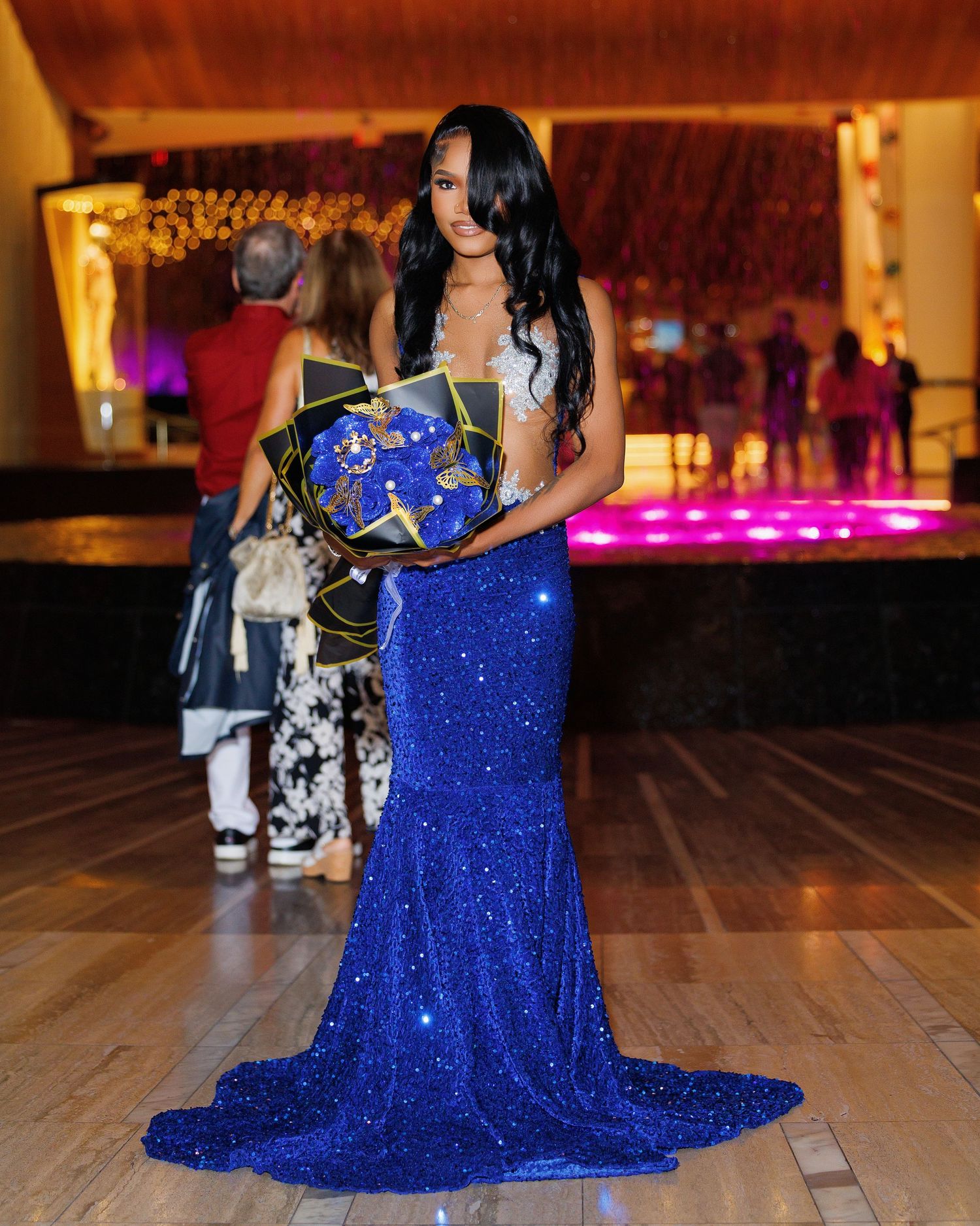 Woman in royal blue sequin mermaid gown holding decorated box at formal event.