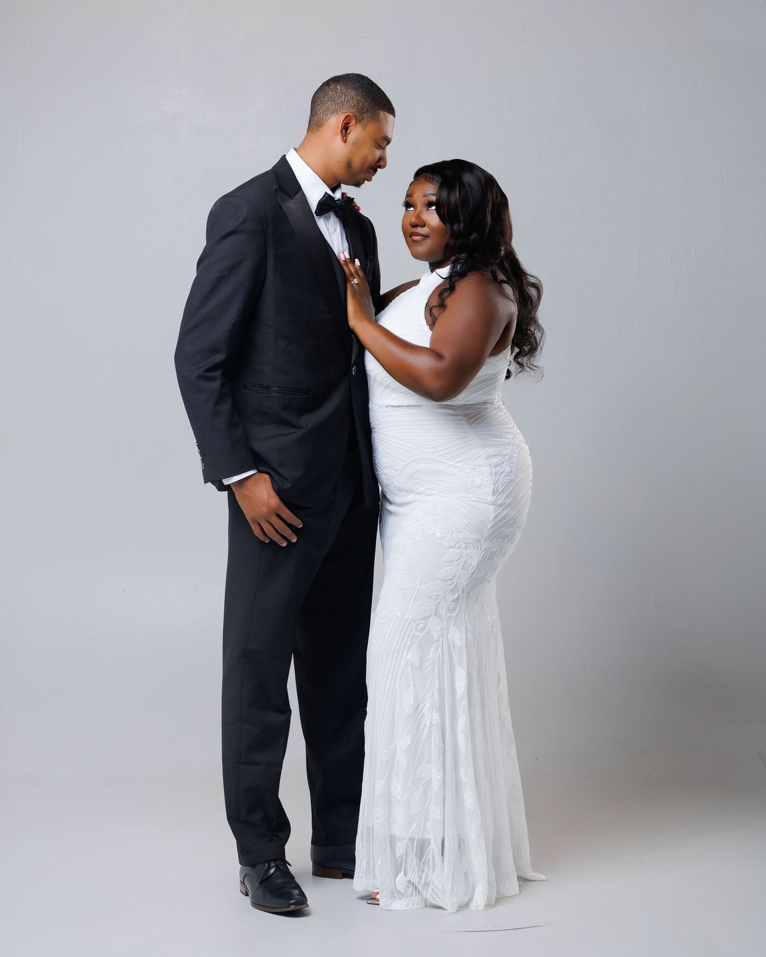 Elegant couple posing in formal wedding attire, man in black tuxedo and woman in white mermaid gown.