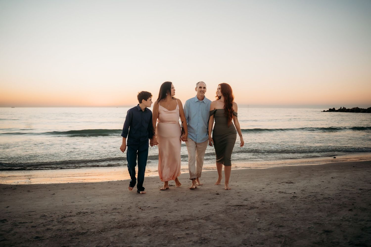 Family of four walking along sandy beach during colorful sunset.