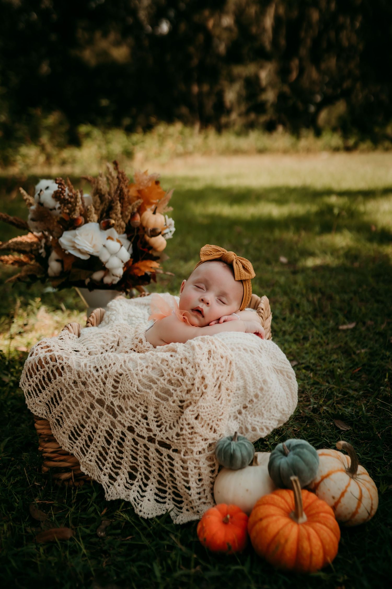 Sleeping newborn baby in crochet basket surrounded by autumn pumpkins and fall decor outdoors.