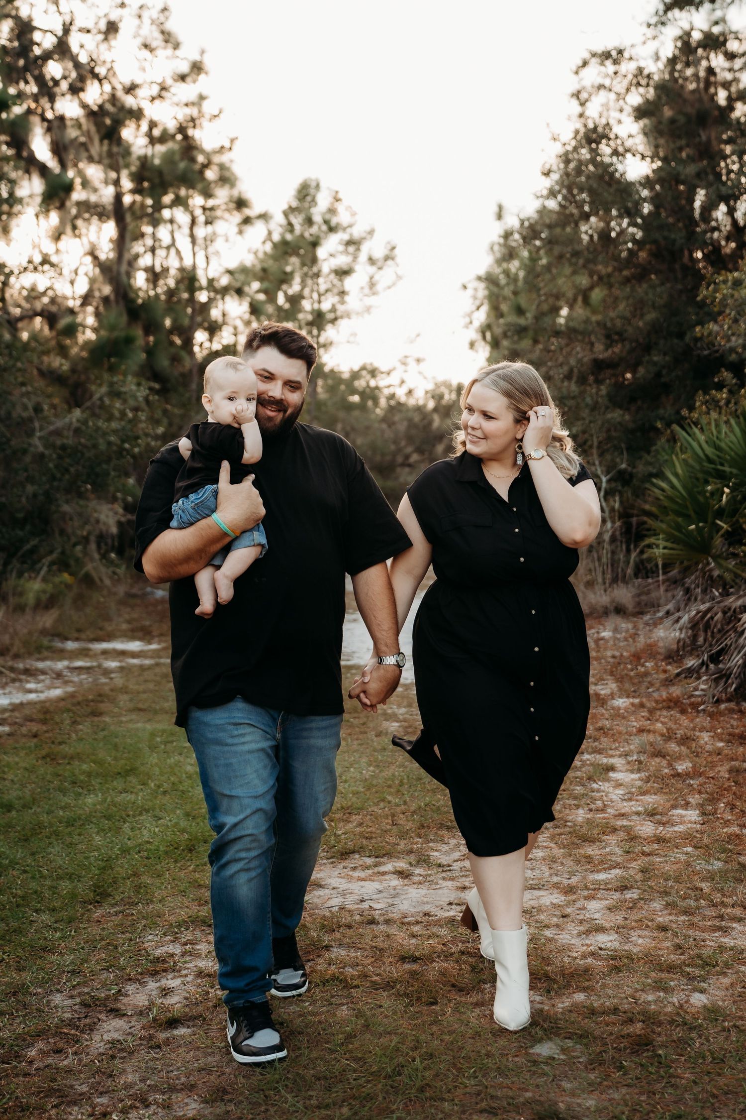 Happy couple in matching black outfits walks outdoors while carrying their baby.