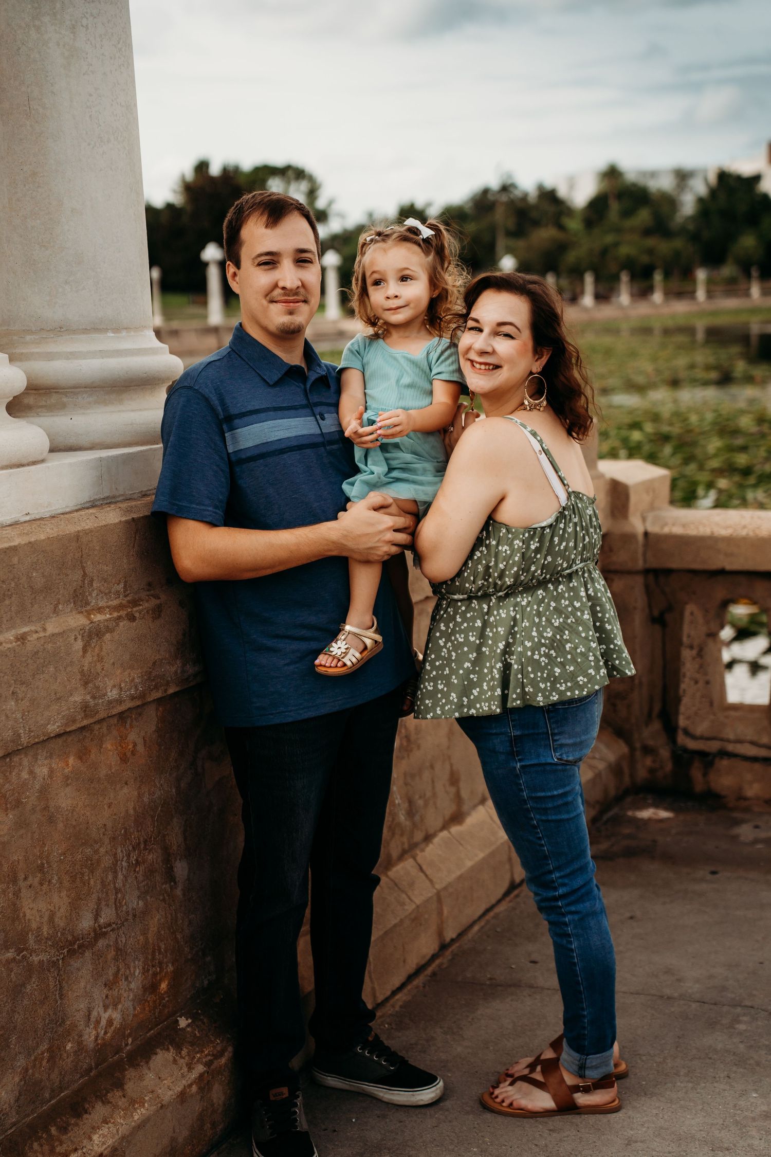Family of three posing together by a stone column in an outdoor setting.