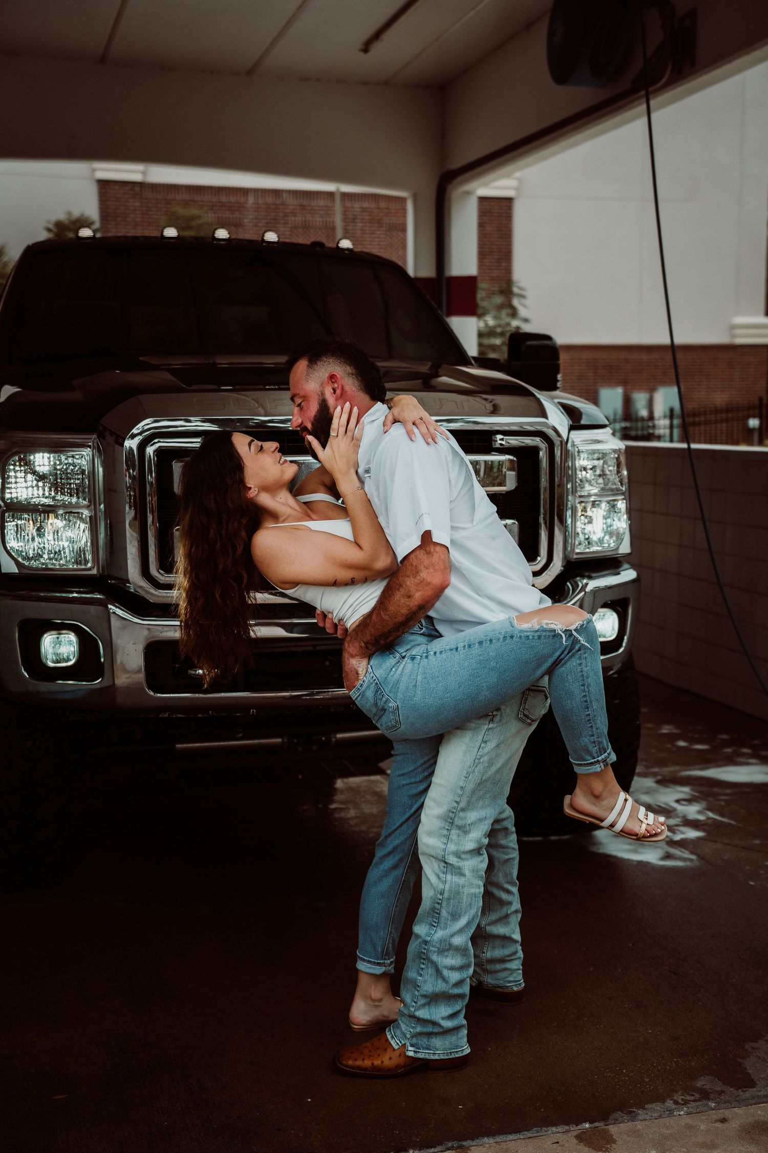 Couple sharing a passionate dip kiss in front of black Ford truck at car wash.