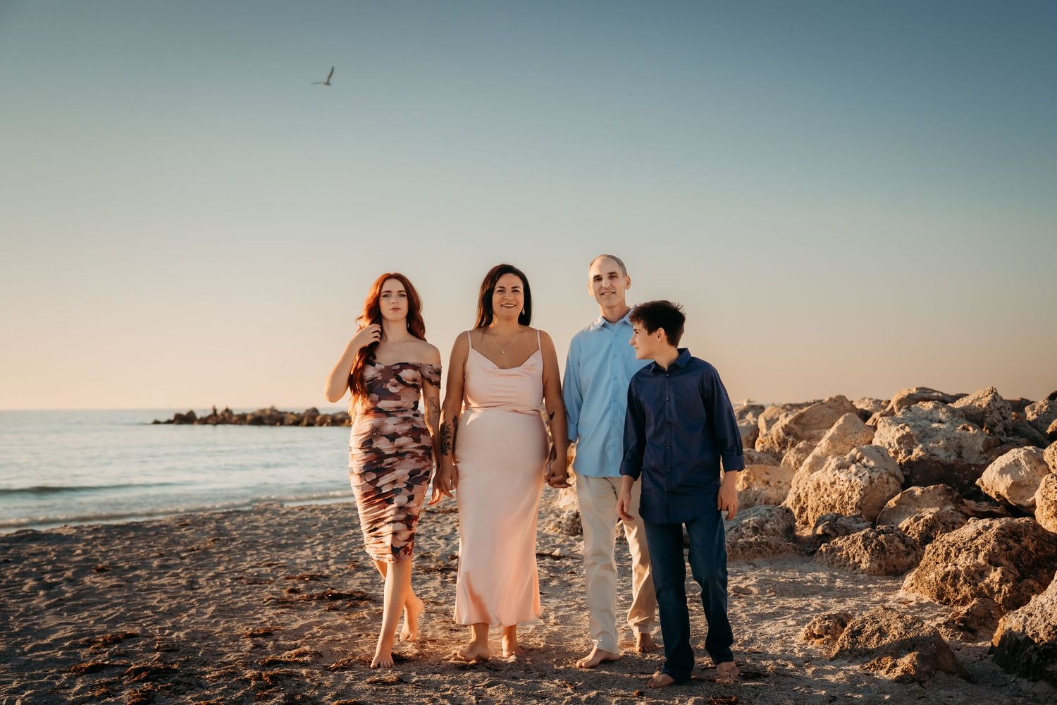 Family of four posing on rocky beach at golden hour sunset.