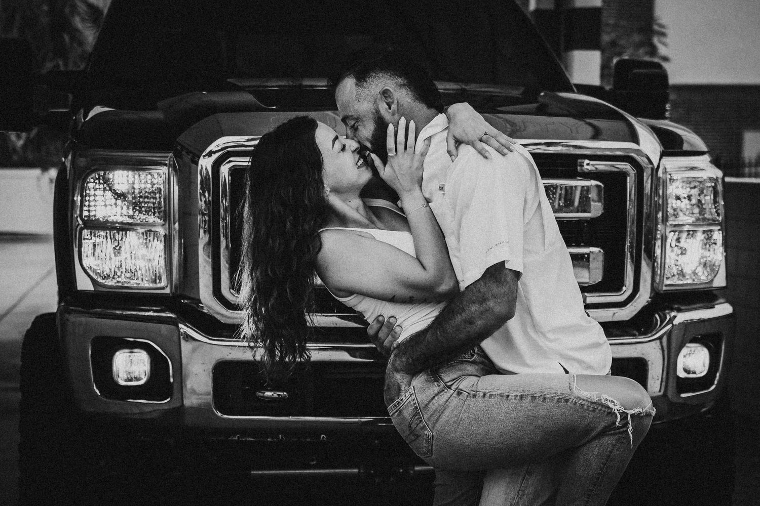 Black and white romantic couple kissing in front of large black Ford pickup truck.