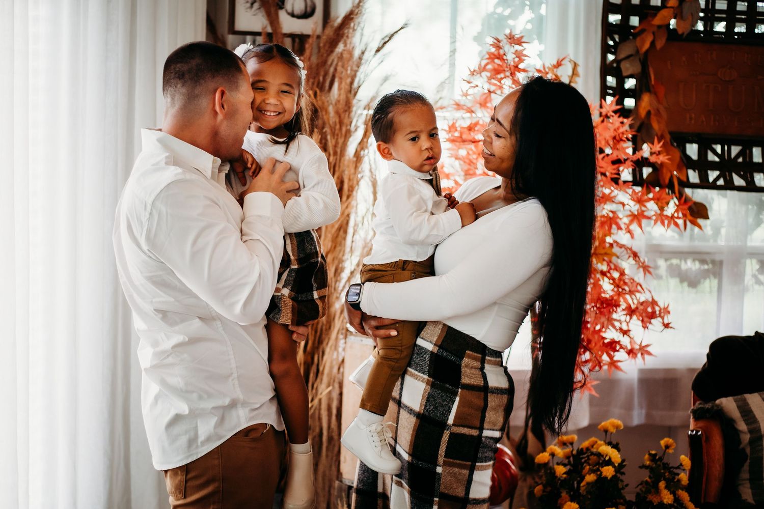 Joyful family of four in matching outfits, parents holding young daughters during fall holiday celebration.
