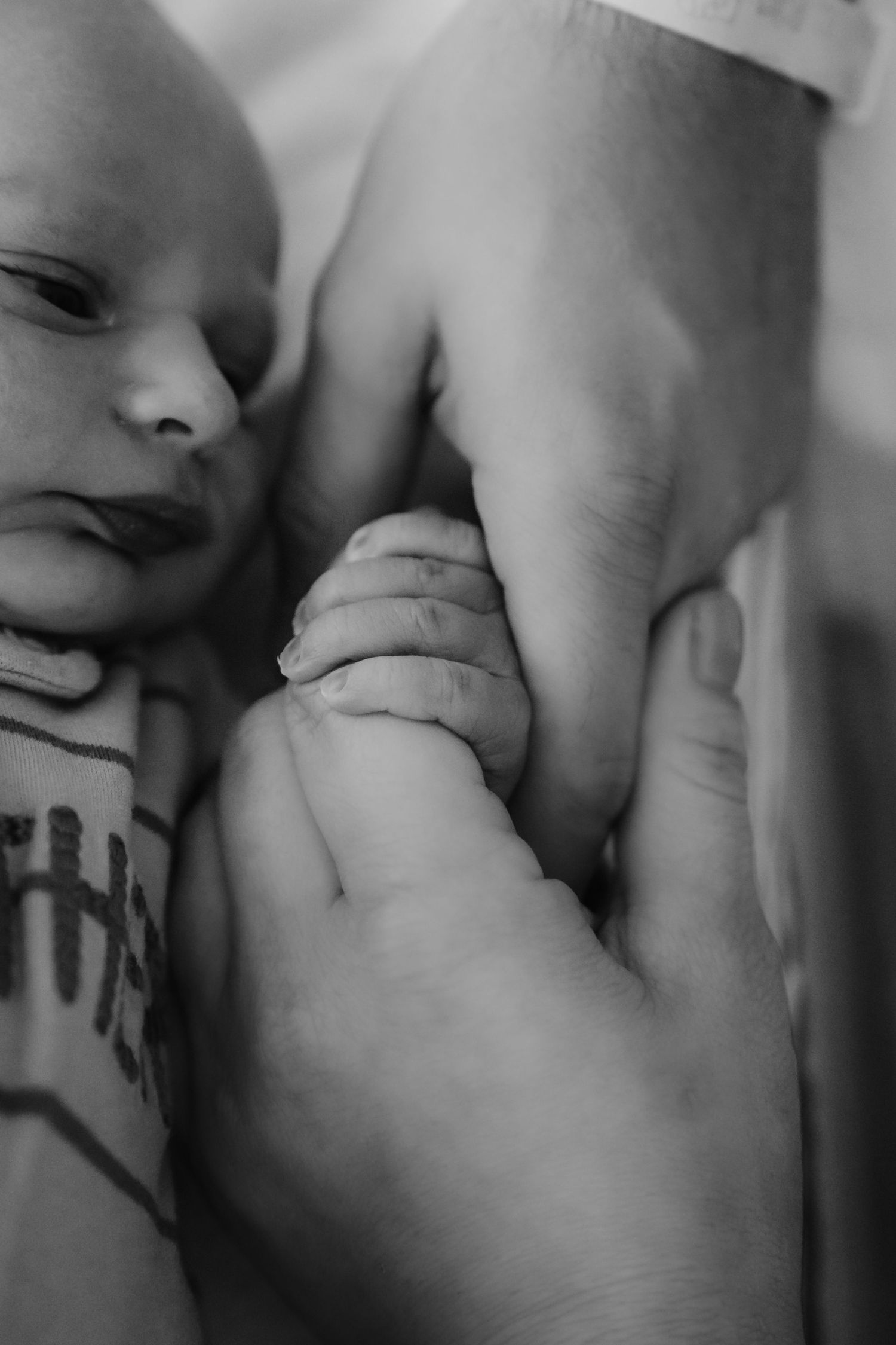 Black and white close-up of a newborn baby gripping an adult's finger tenderly.