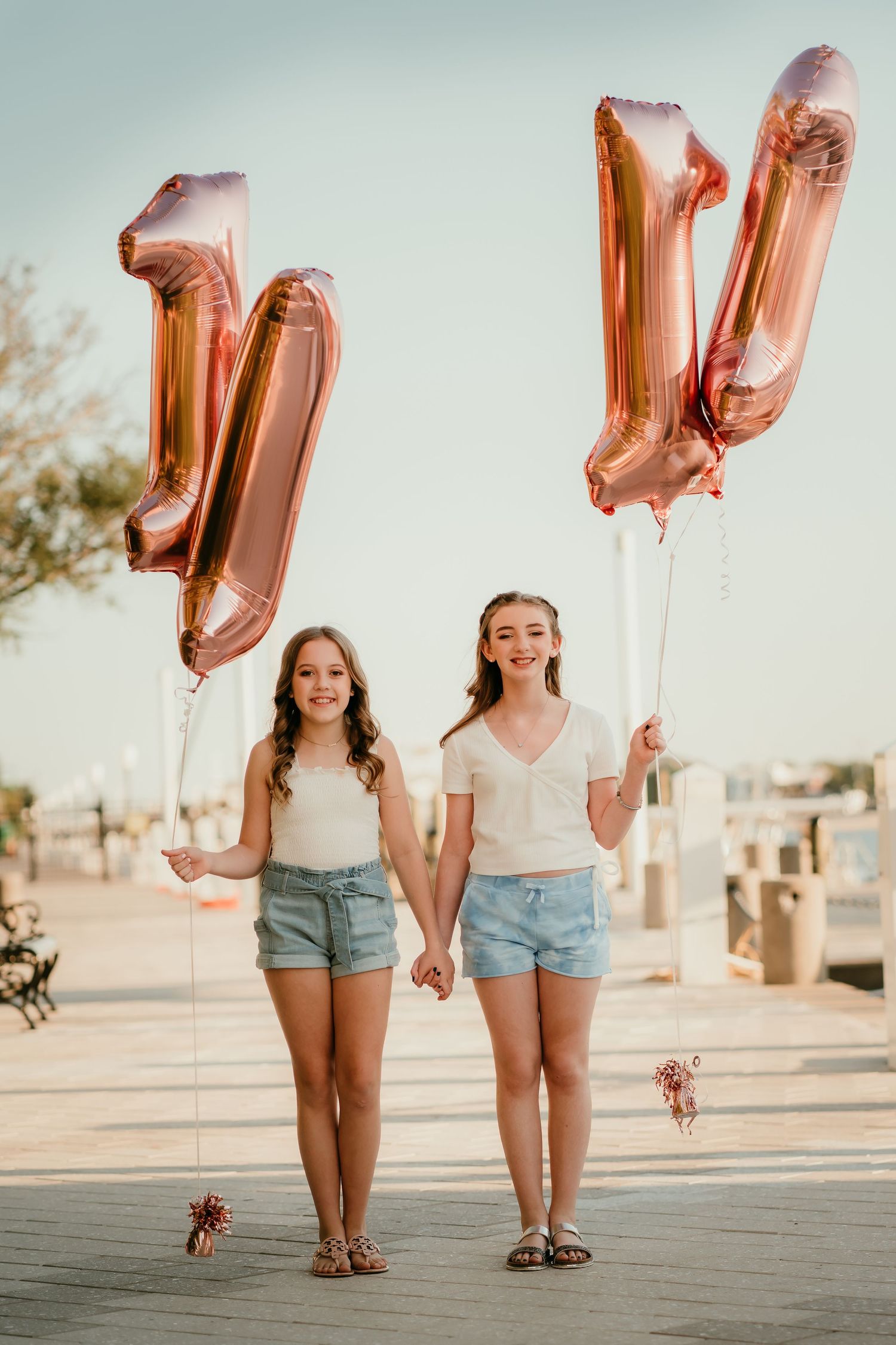 Two girls holding rose gold number balloon bouquets outdoors, celebrating their 11th birthday.
