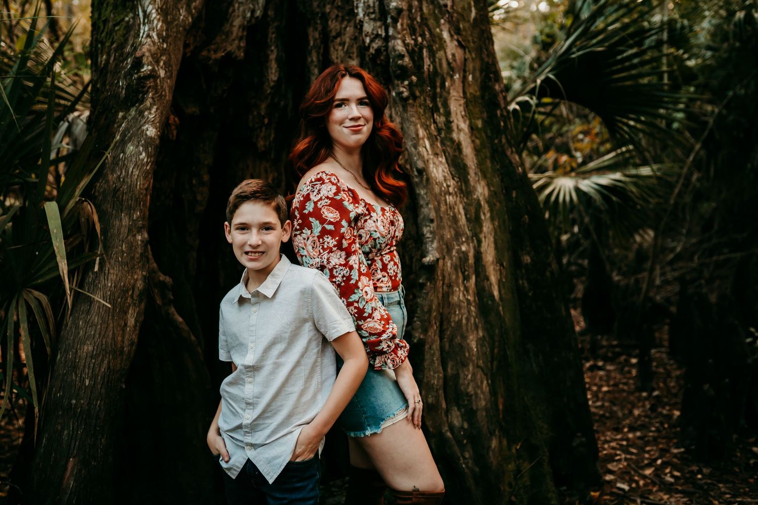 Redhead woman and young boy posing in front of large tree.